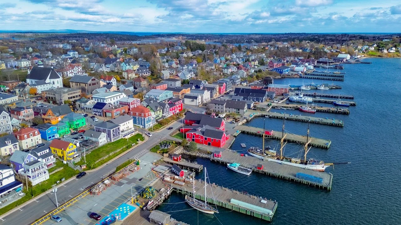 Aerial view of a colorful waterfront town with painted houses, docked boats, and marinas along the harbor.