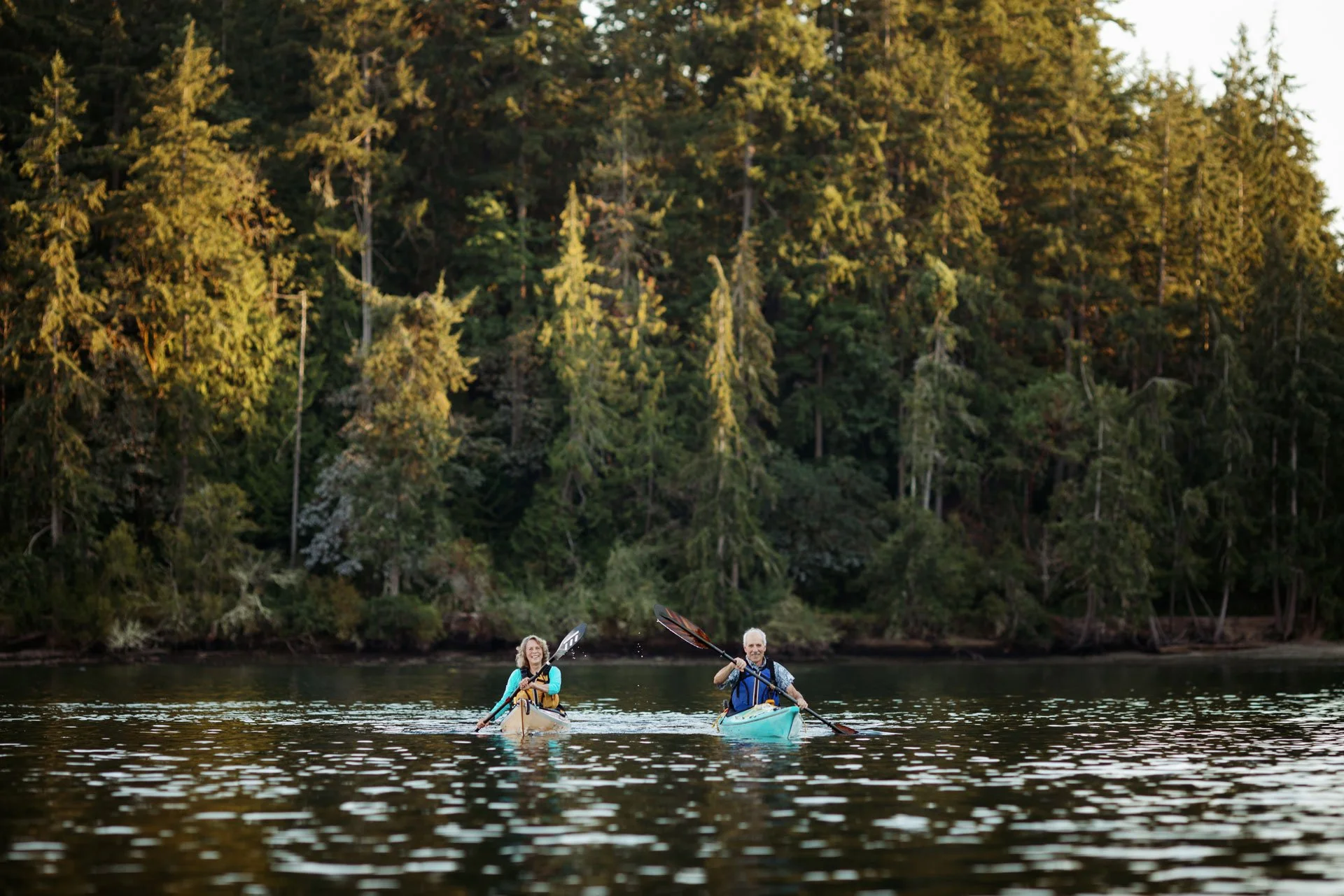 Two people kayaking on a river with a dense forest in the background.