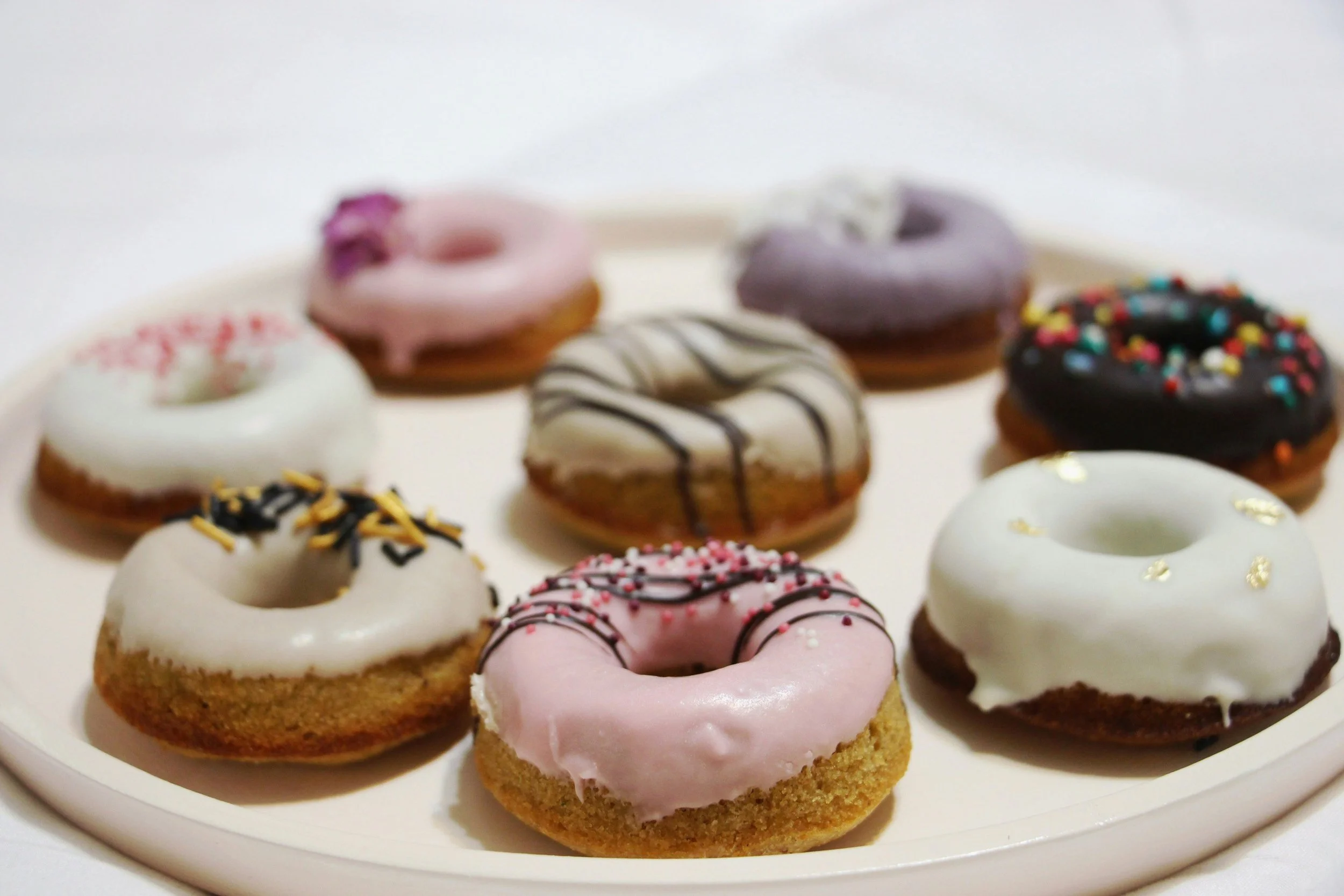 An assortment of donuts with various glazes and toppings on a white platter.