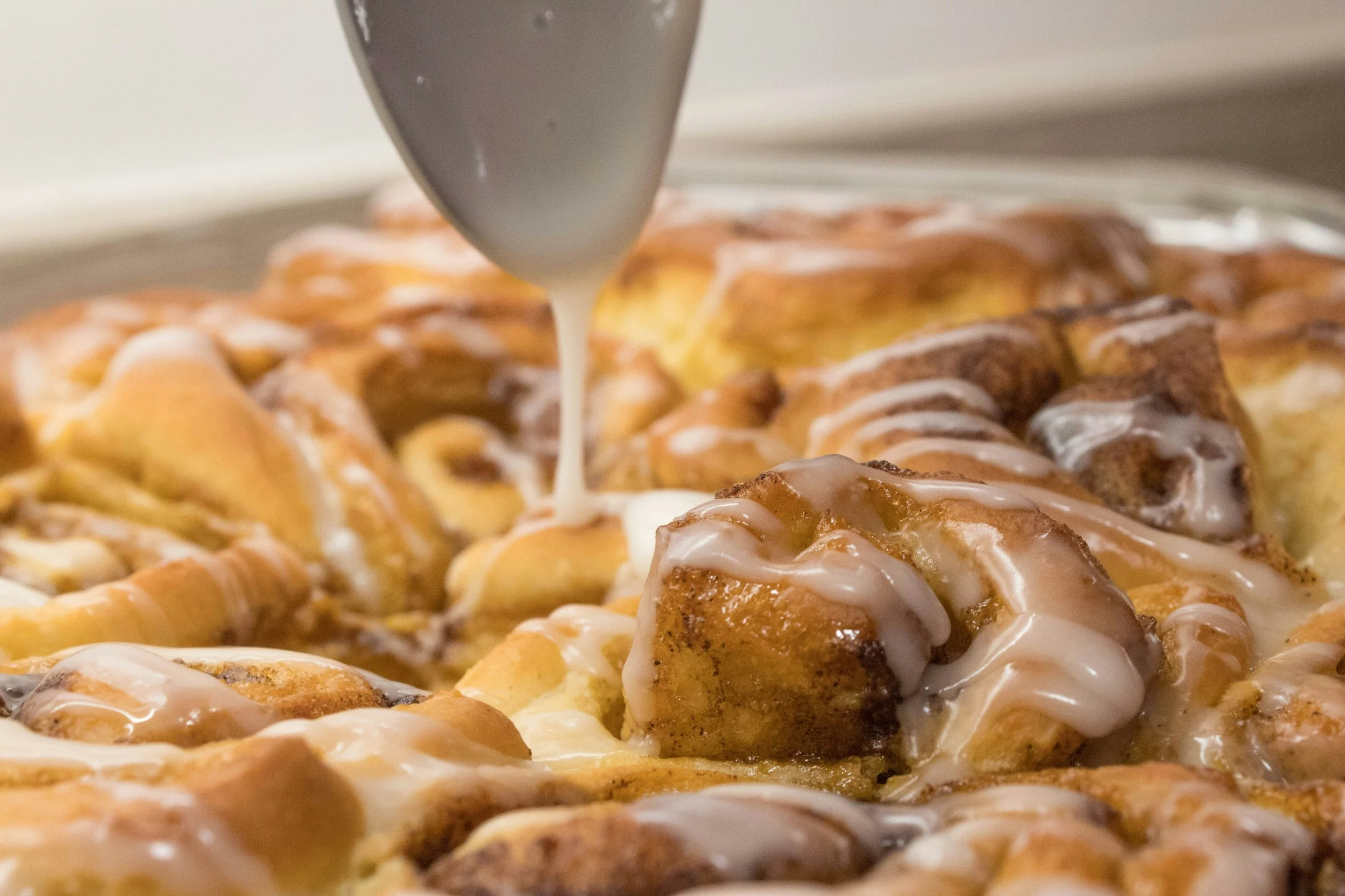 Close-up of a skillet with freshly made cinnamon rolls being drizzled with white icing.