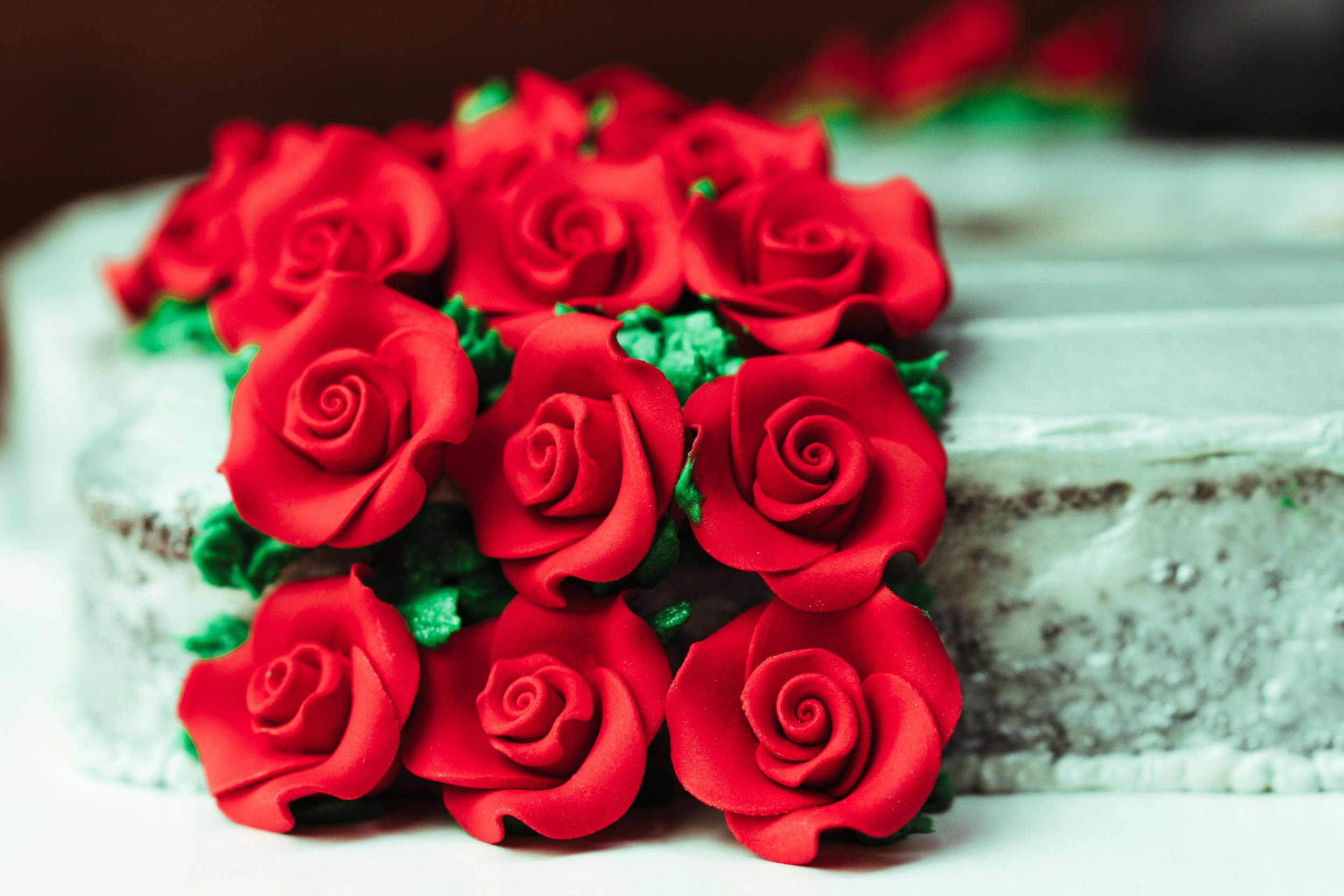 A cake decorated with red rose-shaped icing and green leaves, with a white surface and brown background.