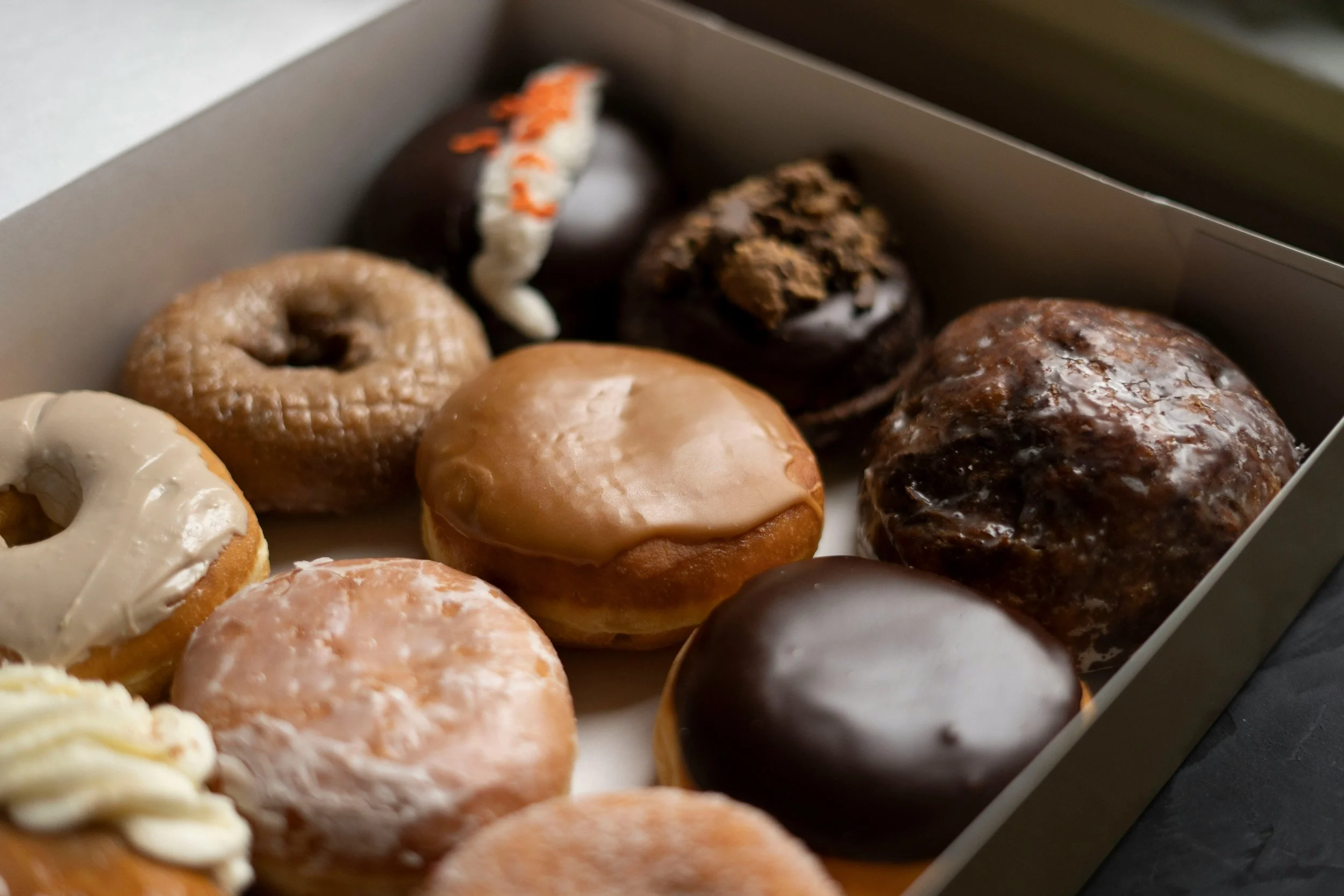 A box of assorted donuts with various toppings and glazes, including chocolate, caramel, and sprinkles.