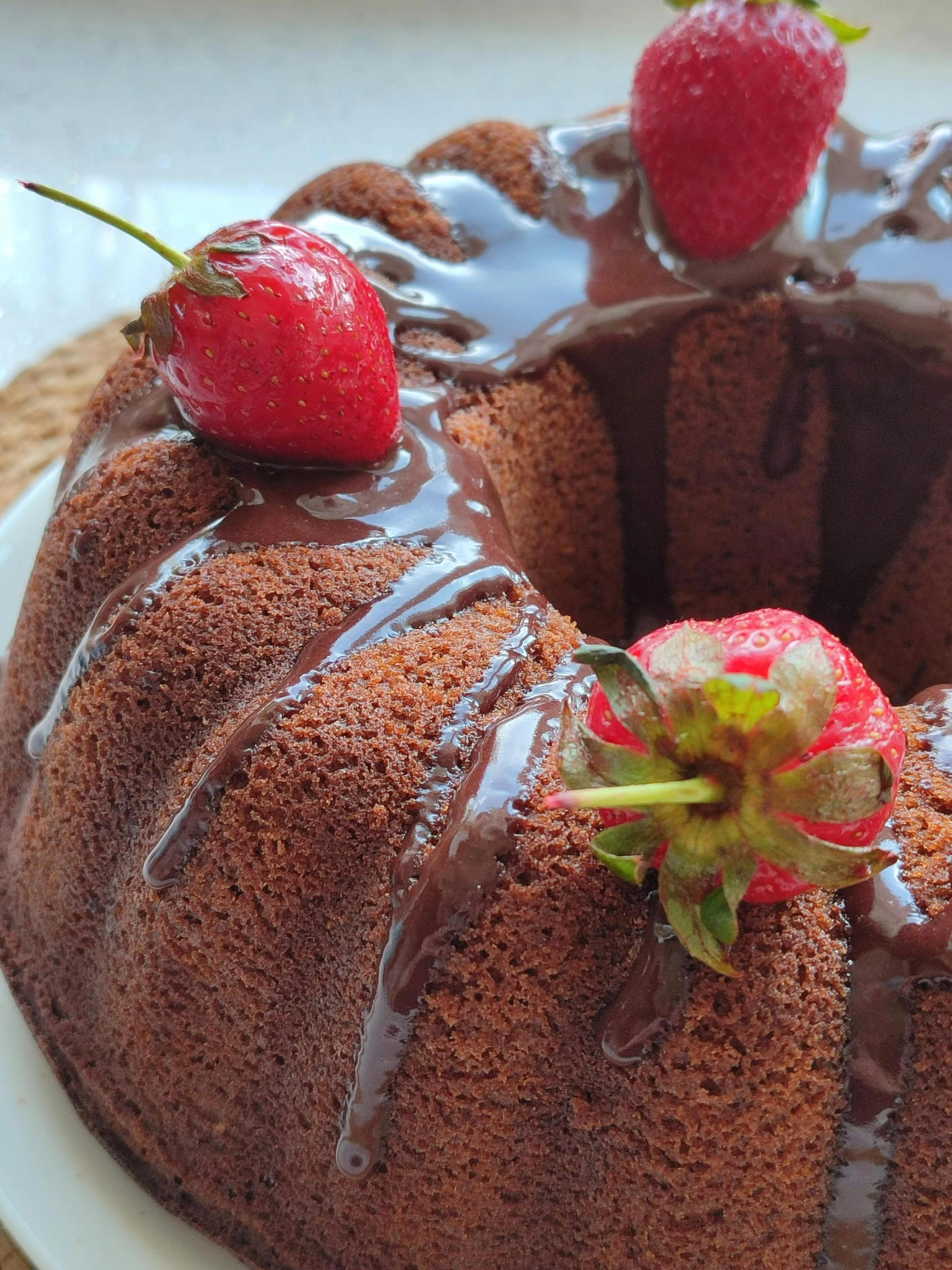Close-up of a chocolate cake with strawberries on top, drizzled with chocolate syrup.