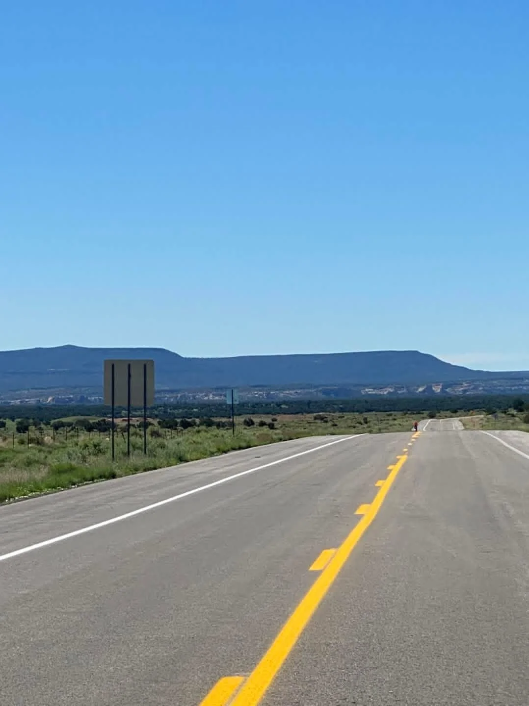 Empty road stretching into the distance with mountains in the background under a clear blue sky.