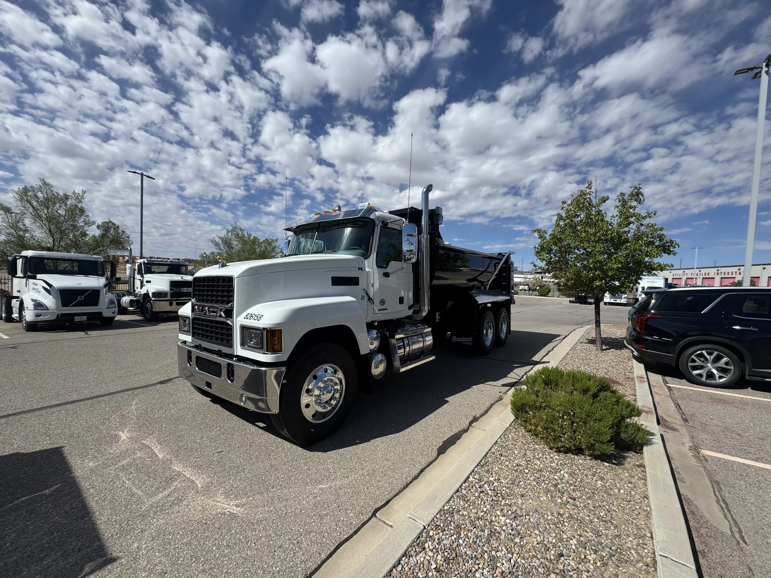 A parking lot with several white trucks parked, a black and white truck in the foreground, small trees and a building with a sign that reads 'TULSA TRAILER INTERSTA' in the background, and a cloudy sky overhead.