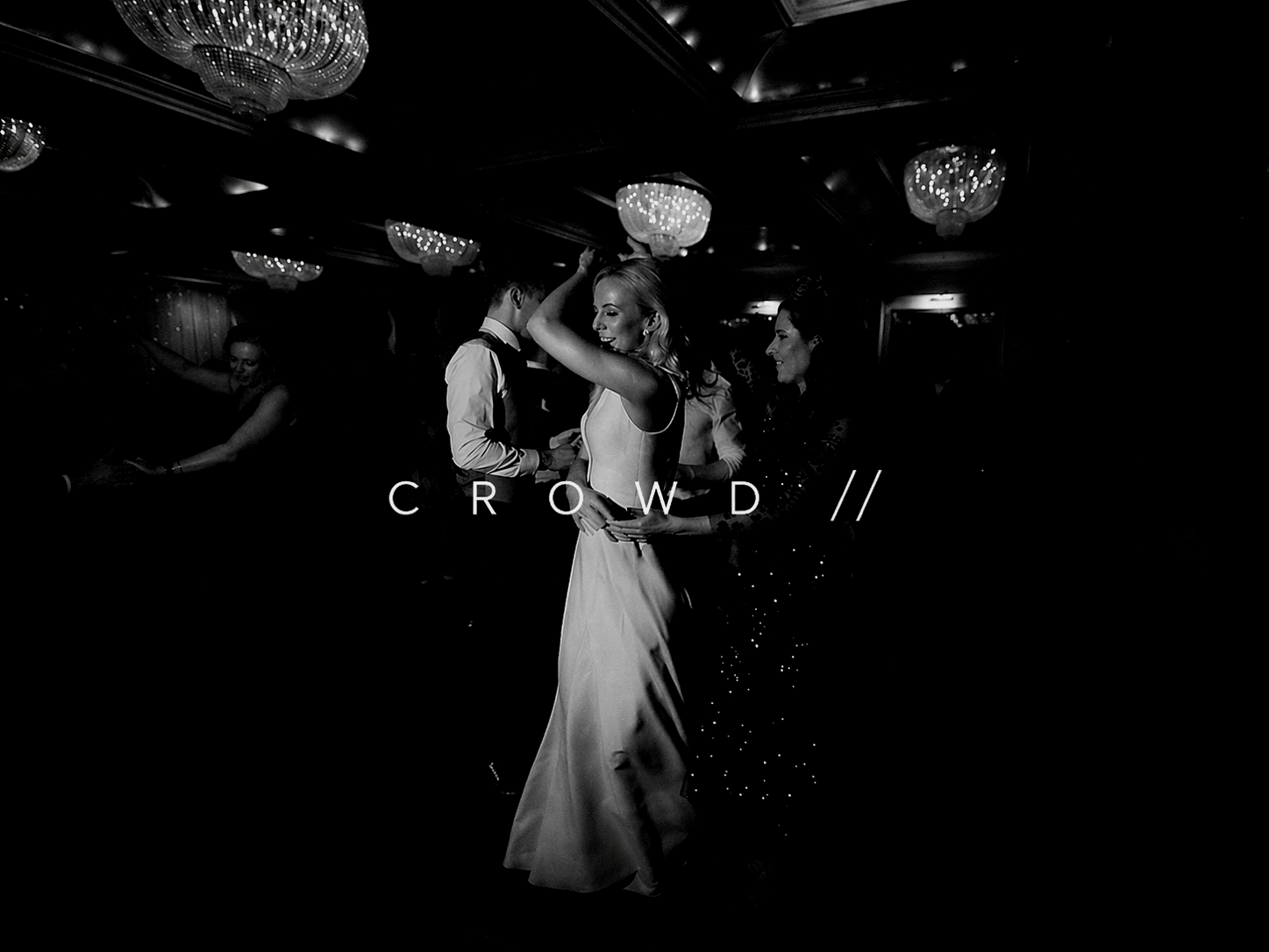 Black and white photo of a bride dancing with guests at a wedding reception, chandeliers hanging from the ceiling, with the word "CROWD" overlaid.