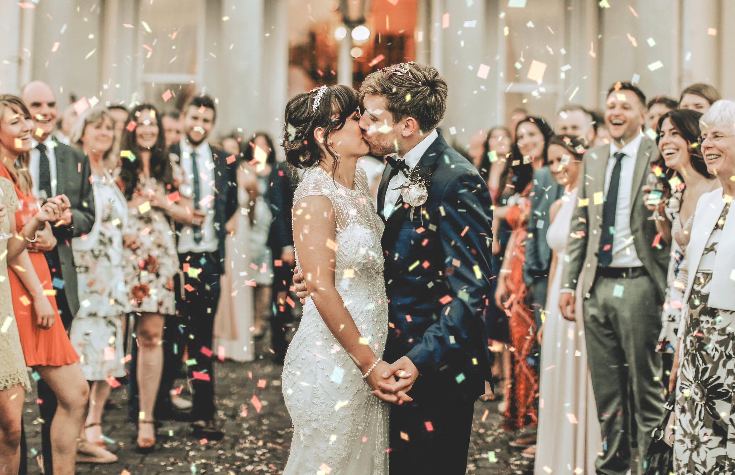 A bride and groom kissing at their wedding reception, surrounded by guests and falling confetti at Moyvalley Co Meath