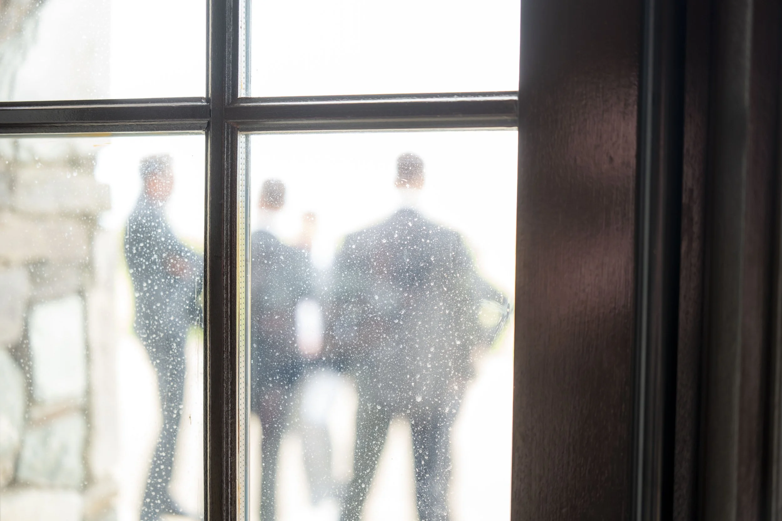 Indoor view through a rain-speckled window with two blurred figures outside.