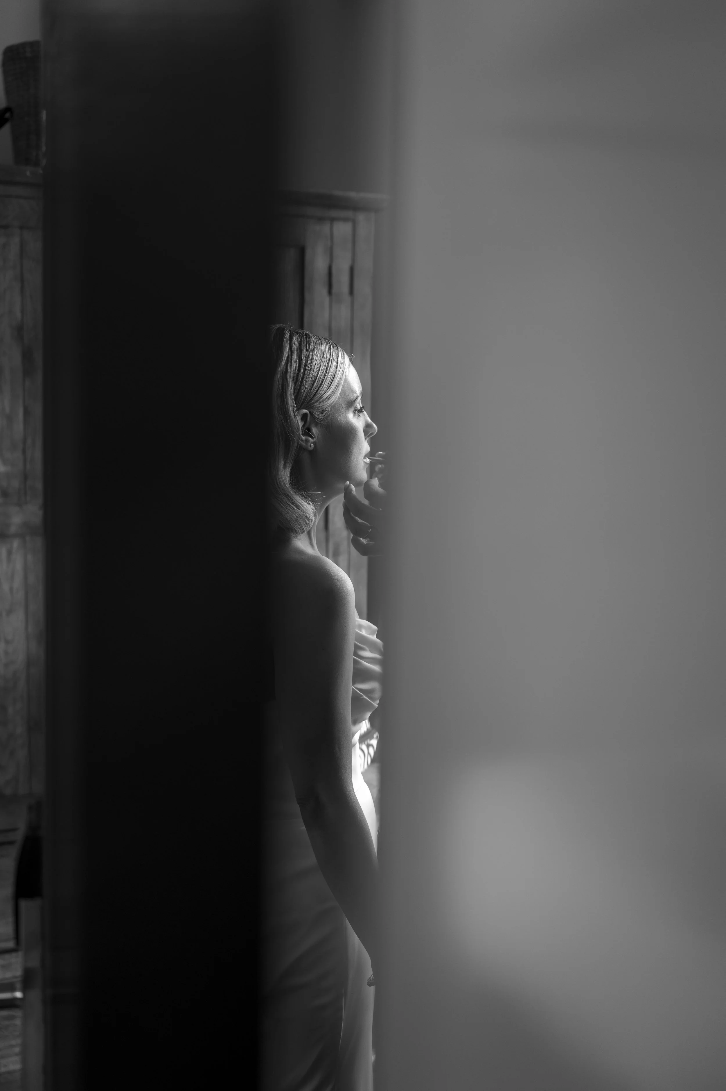 A woman with blonde hair looking out a window, black and white photo, indoors with wooden wall panels.