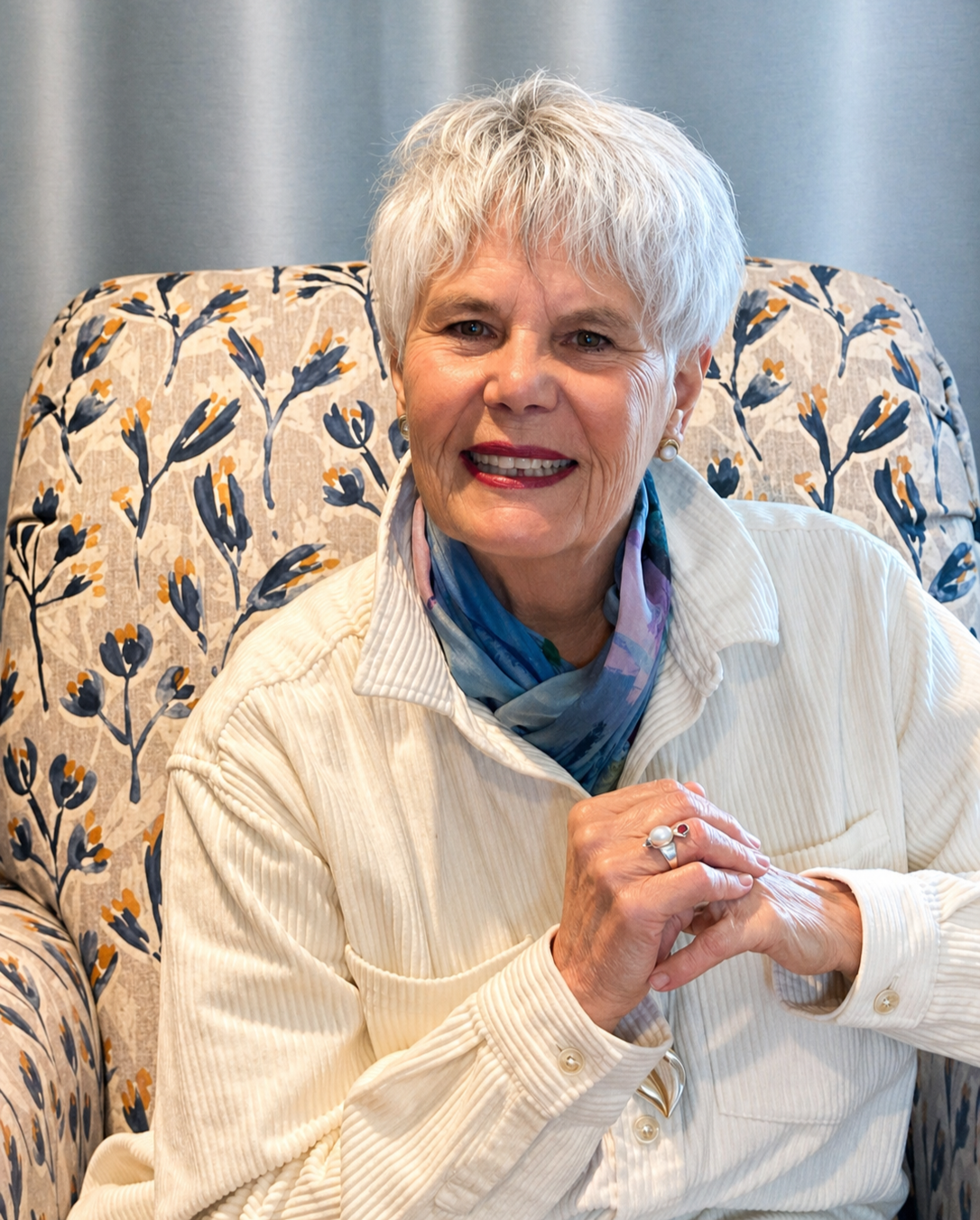 Terra  seated in a floral armchair, smiling with quiet warmth.