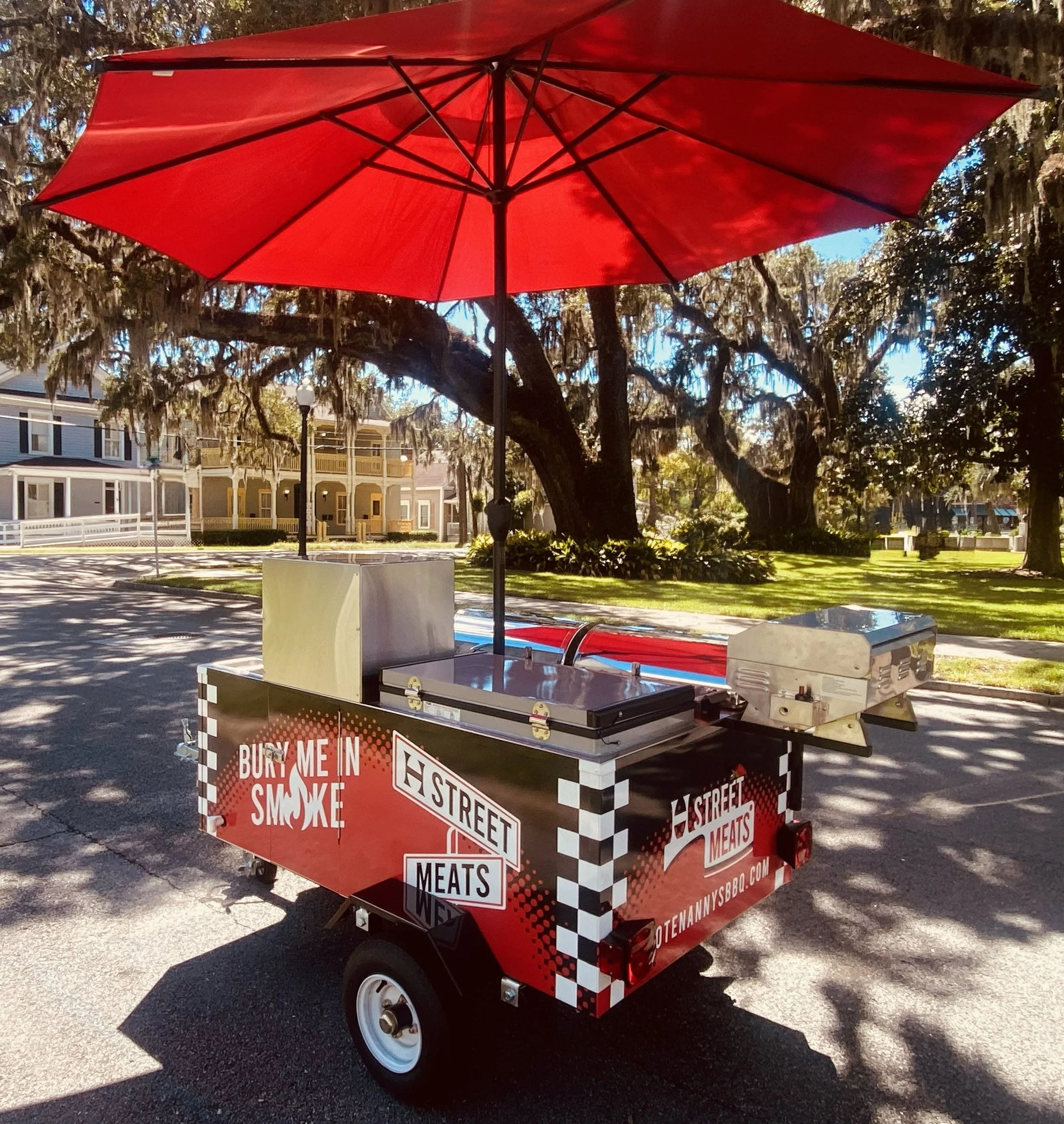 H Street Meats cart by Hootenanny's BBQ with a checkered black-and-white pattern, advertising meats and street food, parked outdoors under trees with residential buildings in the background.