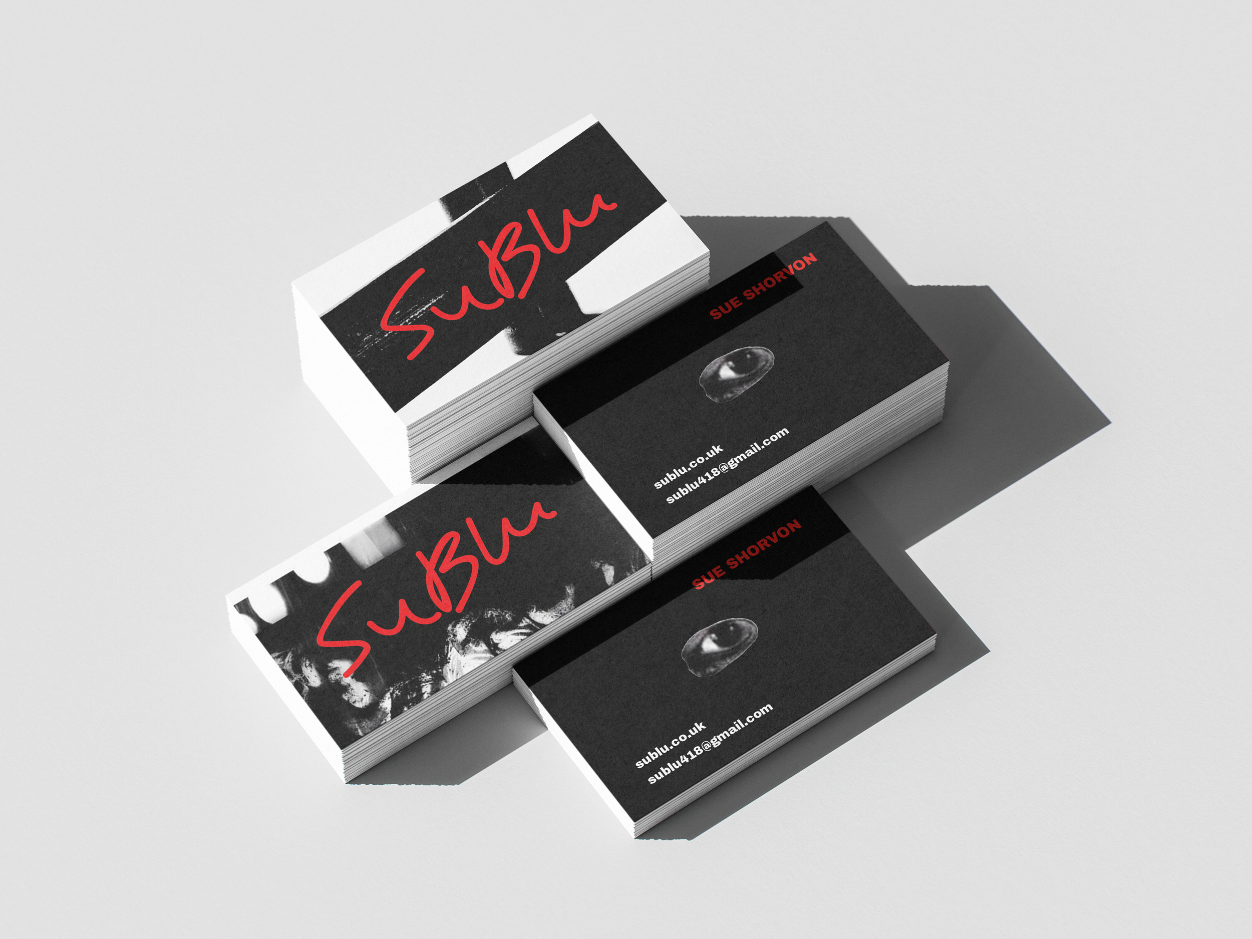 Stack of business cards with black, white, and red design, featuring the word "SuBlu" in red handwriting style and contact information in white and red text.