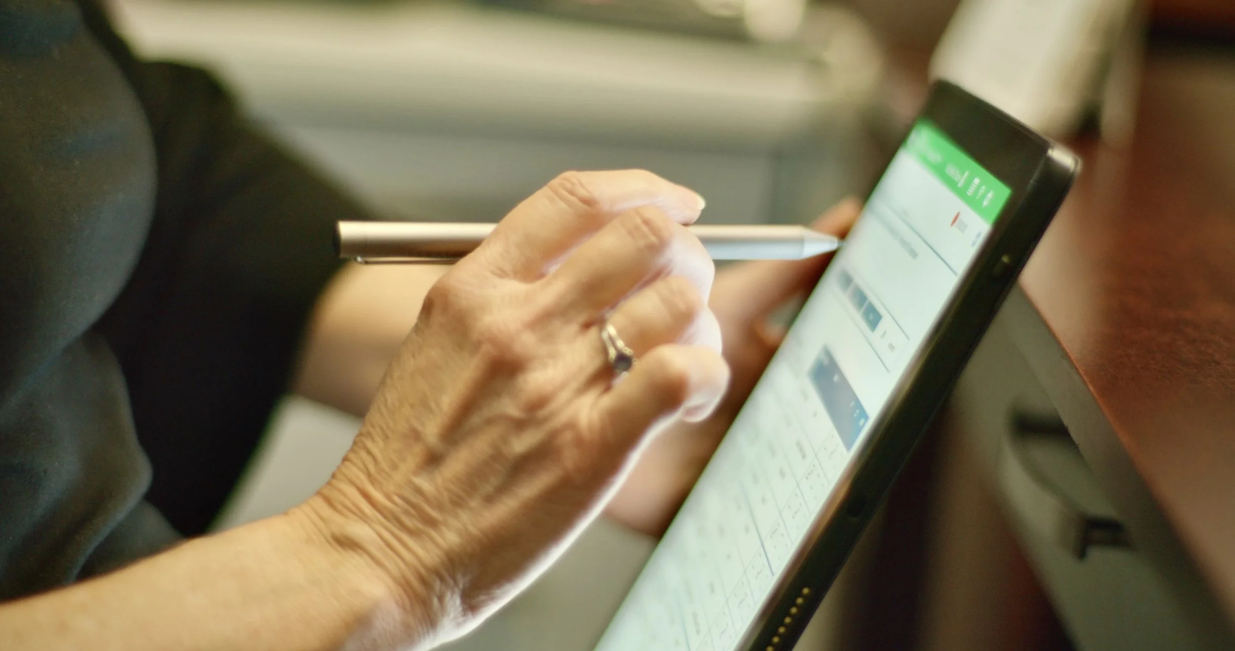 Close-up of an elderly person's hand using a smartphone, holding a stylus and browsing a website or app.