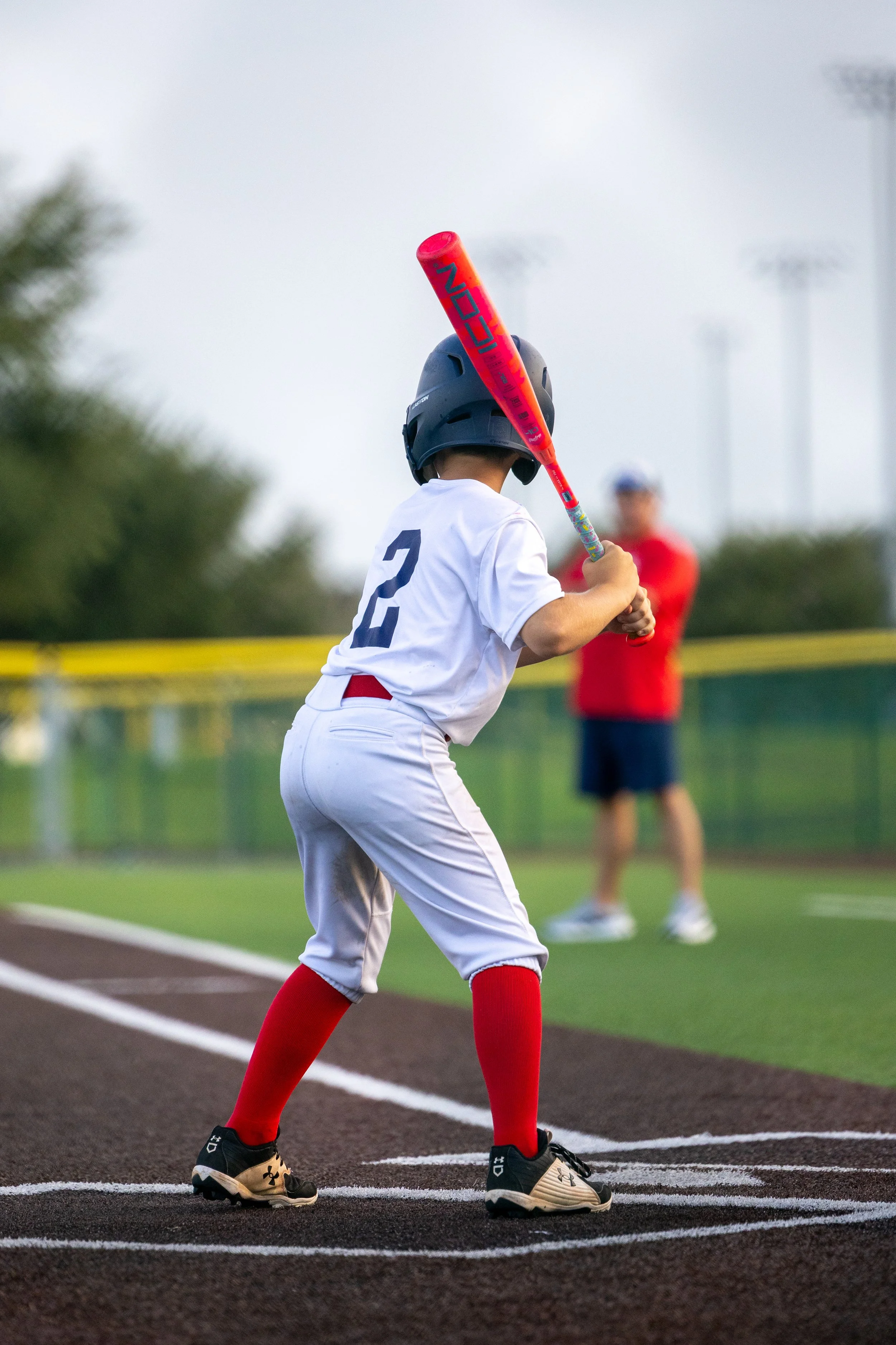 A young baseball player in uniform, wearing a helmet, holding a bat, and standing on a base at a baseball field.