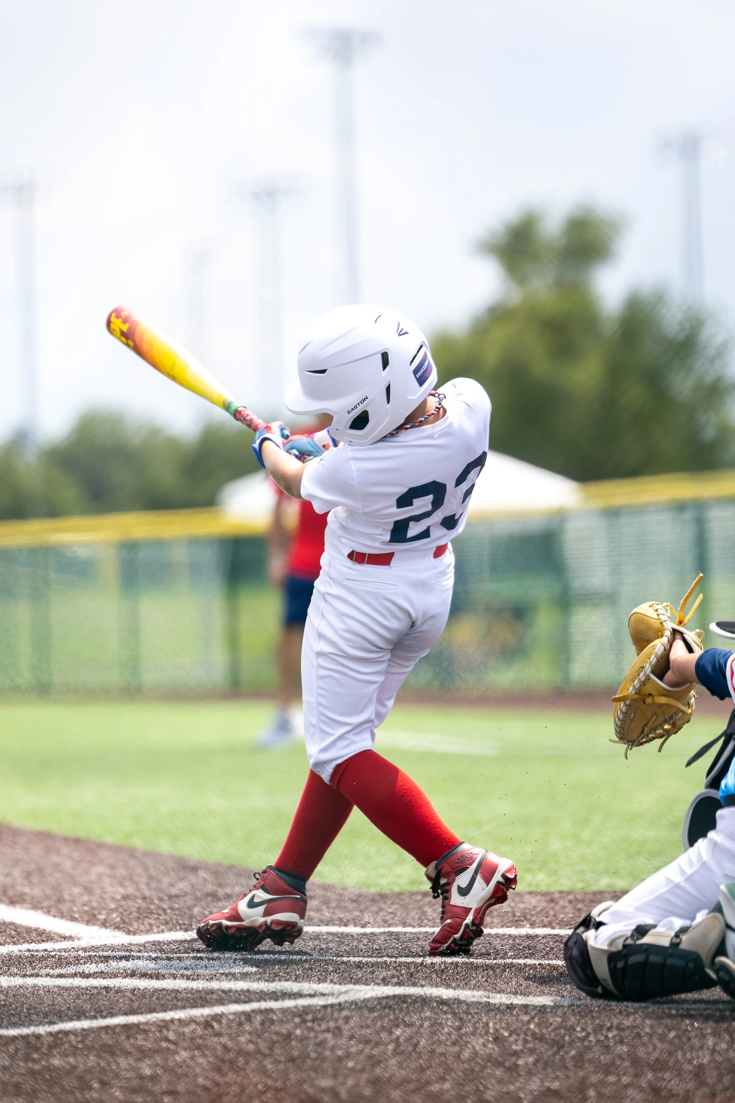 Youth baseball player in white uniform and helmet swinging a bat at the ball on a baseball field.