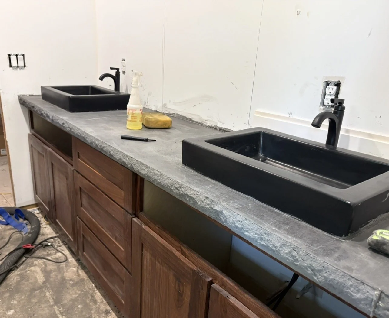 His and hers bathroom sink renovation with two modern black sinks installed in a concrete countertop, with dark wooden cabinets.