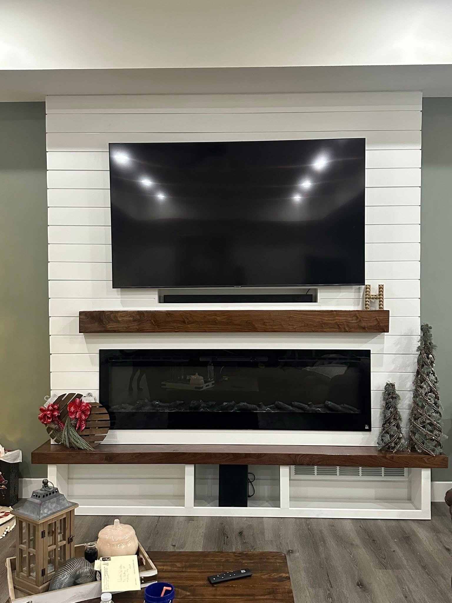 A living room with a modern white fireplace wall, a wooden mantel, a large flat-screen TV mounted on the wall.