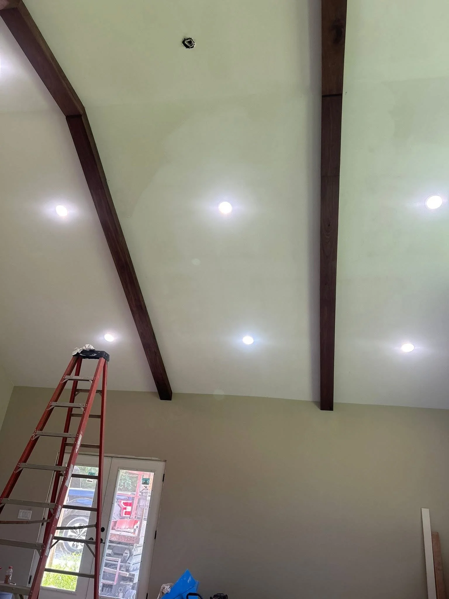 The interior of a room with a high ceiling featuring two dark wooden beams and recessed ceiling lights.
