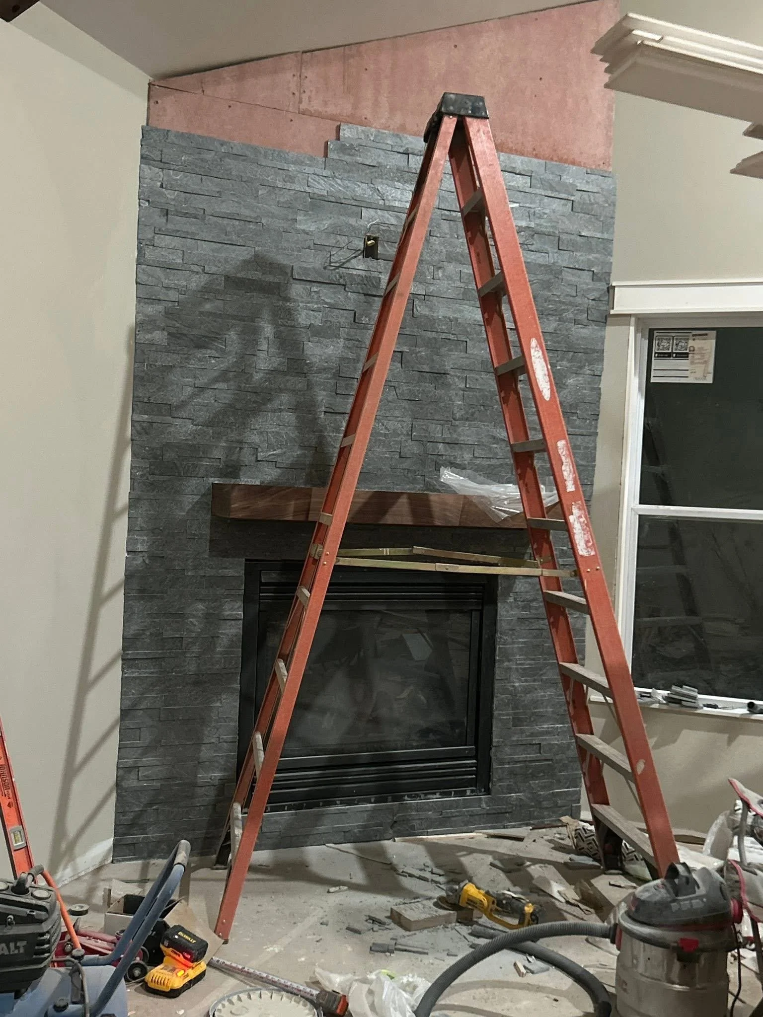 Interior of a room under renovation showing a grey stone wall with a fireplace.