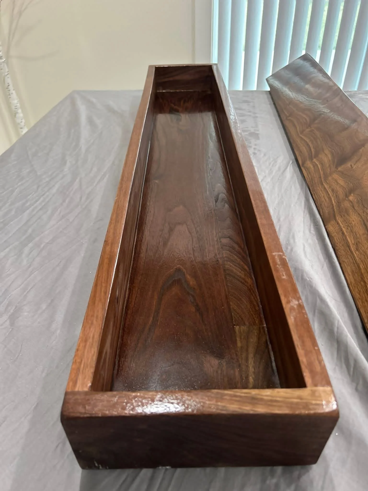 A rectangular wooden beam with raised edges, glossy finish, and a rich brown wood grain pattern.