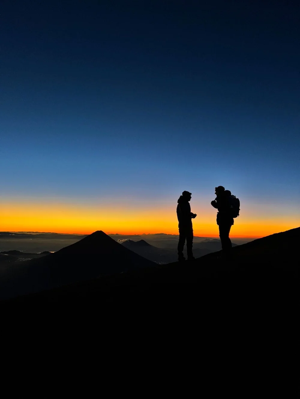 Two hikers at dawn above the clouds