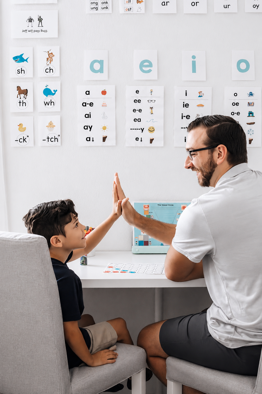 Michael Lavery giving a high five to a student in a classroom with educational posters on the wall, including phonics charts and word families.