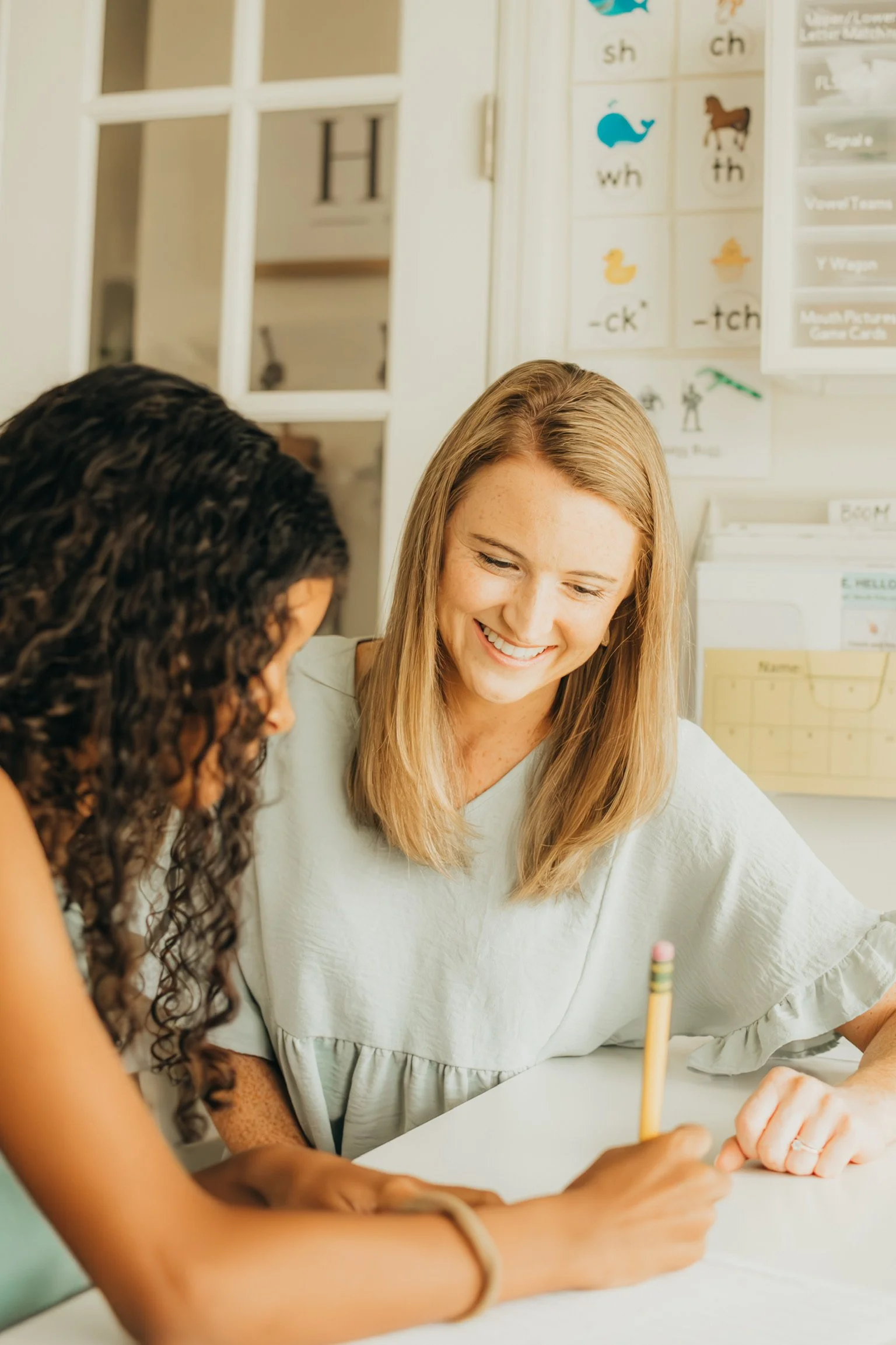 Emily Lavery and a student sitting at a desk, writing, with educational posters on the wall.