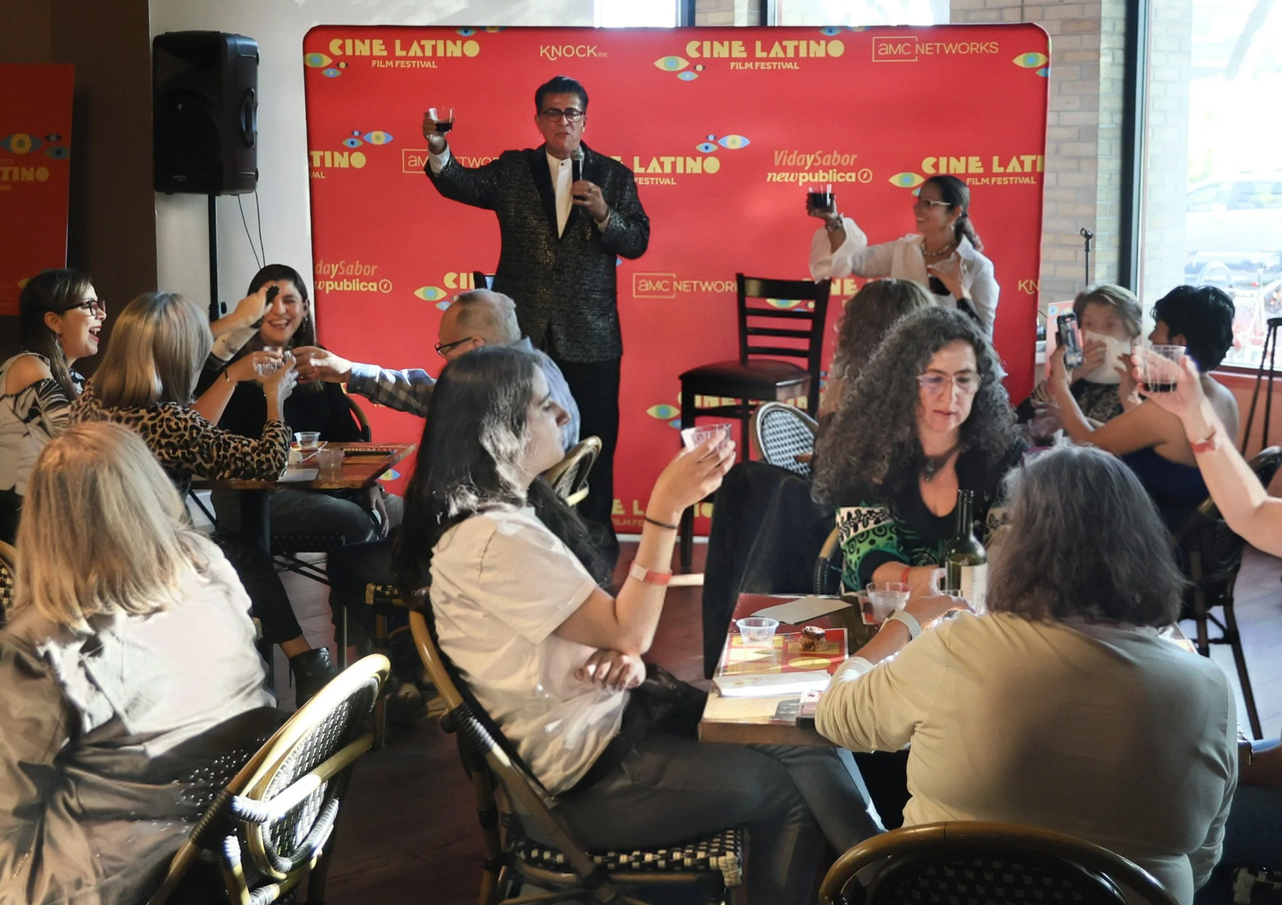 Rico toasting during a wine and chocolate tasting, with the audience sitting around tables. An event during 2025 Cine Latino in Minneapolis.