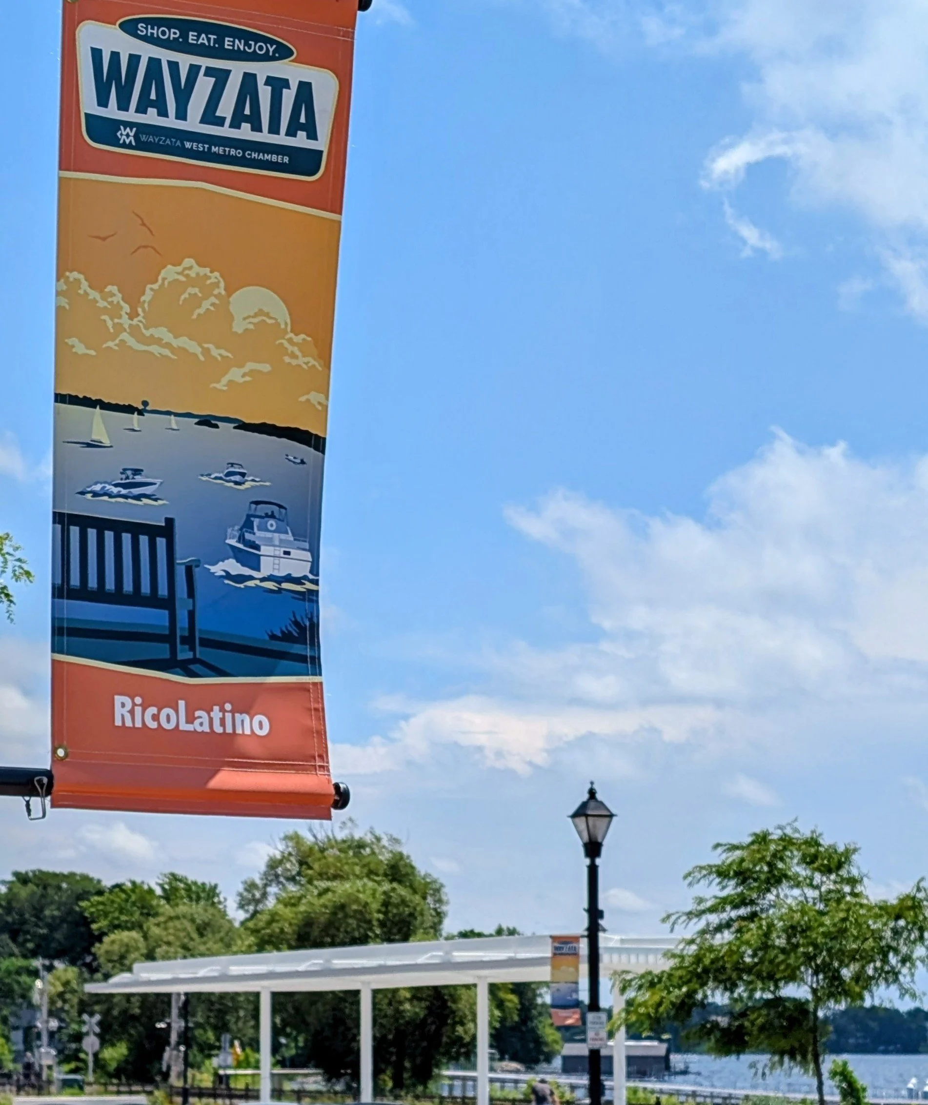 Wayzata chamber of commerce banner with the RicoLatino name on it. The banner is on Lake Street, down Wayzata, Minnesota, across the street from Lake Minnetonka and the panoway.