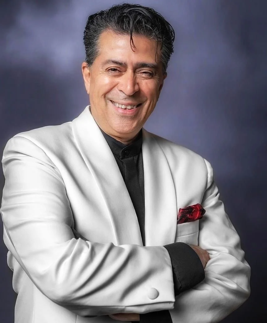 Rico in a white tuxedo smiling at the camera