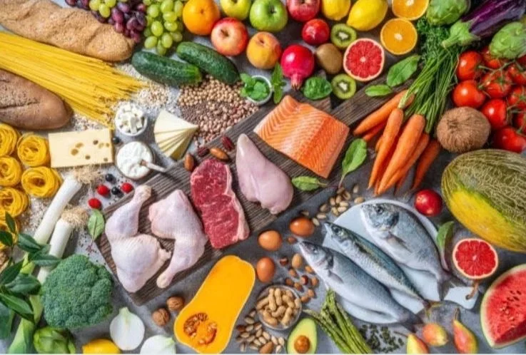 Assorted fresh fruits, vegetables, seafood, meats, pasta, cheese, eggs, and nuts arranged on a table.