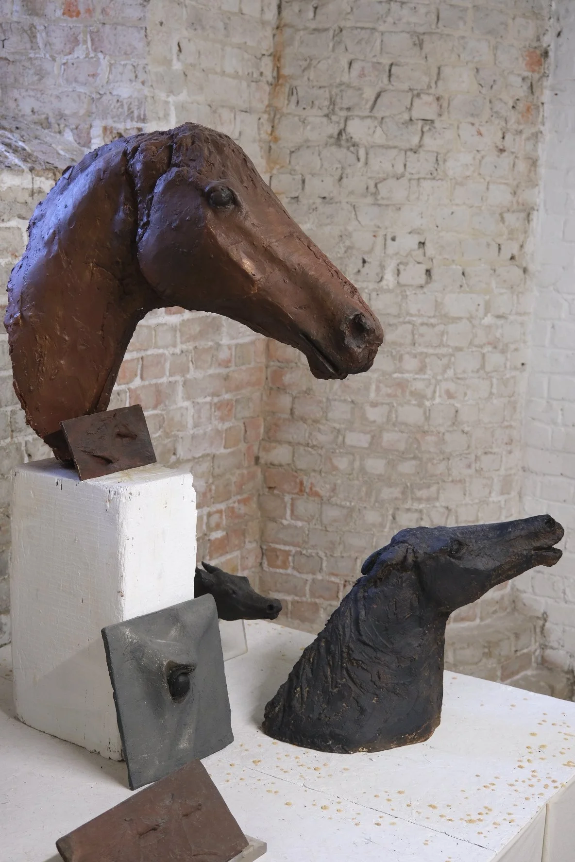 Kunstwerken van paardenhoofden gemaakt van verschillende materialen, tentoongesteld tegen een bakstenen muur.