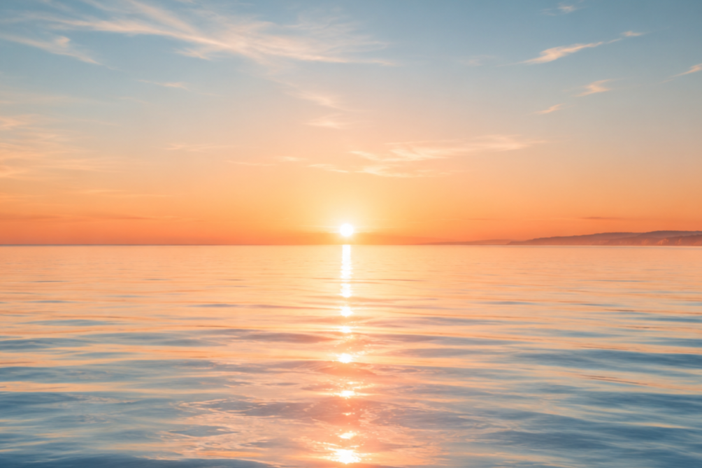 Sunset over calm ocean with a colorful sky and distant land on the horizon.