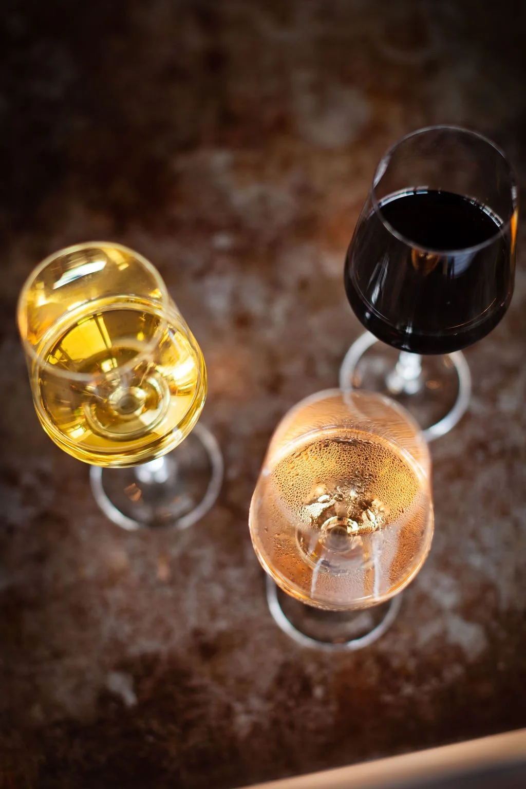 Wine flight from the Cordelle Bar in event space in Nashville Three wine glasses viewed from above on a brown surface, each containing a different type of wine: white, red, and rosé.
