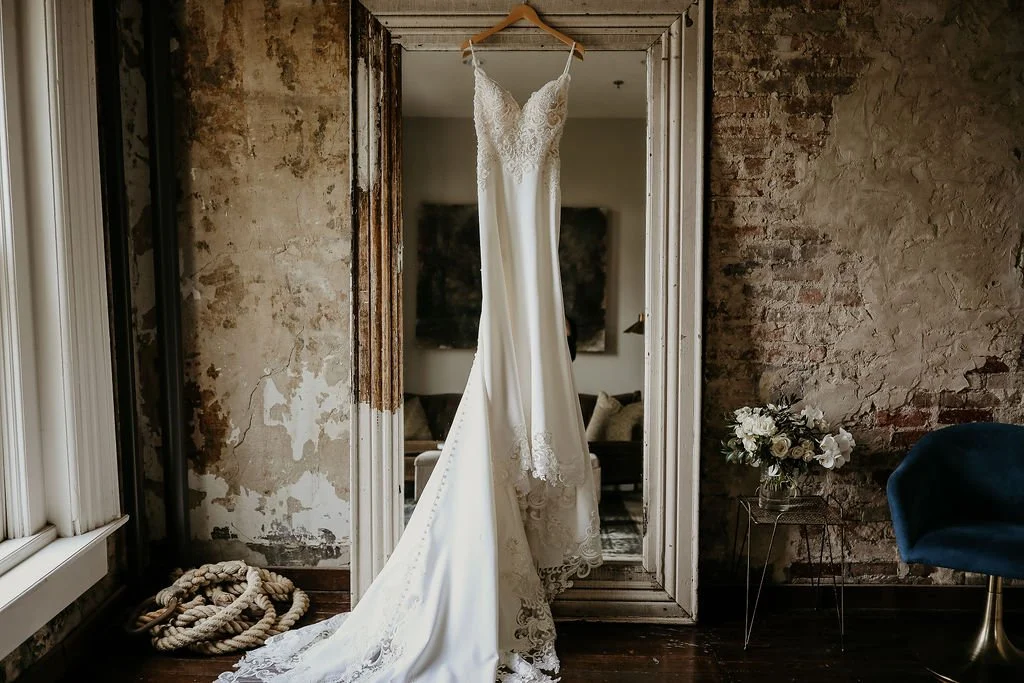 A white wedding dress hanging on a mirror in a rustic, exposed-brick room in the Bridal Suite in Downtown Nashville at the Cordelle with stylish backdrop.