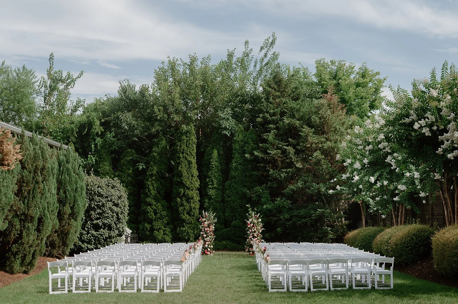 Outdoor wedding cermony setup with white chairs arranged in rows beneath a tree-lined sky, with floral decorations at the aisle entrance in Downtown Nashville.