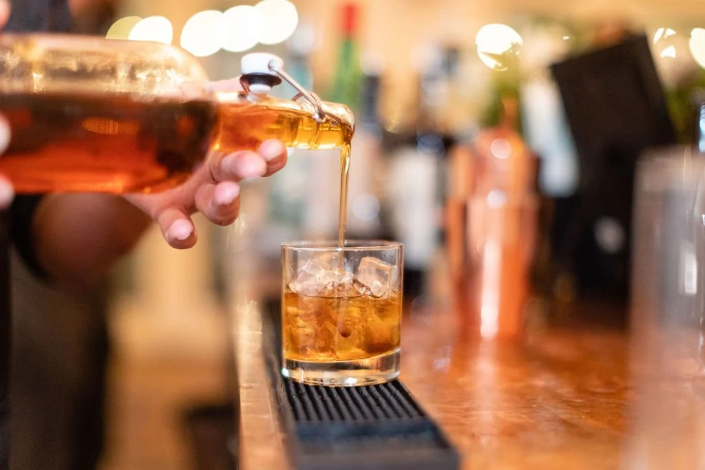 Cordelle Bar Service at an event in Nashville Person pouring whiskey over ice into a glass on a bar counter.