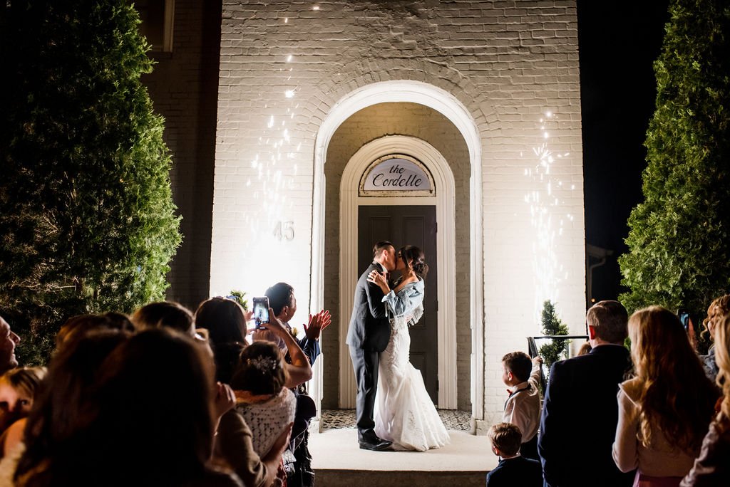 Cordelle in downtown Nashville Couple sharing a kiss during the exit of their wedding ceremony and reception at the Cordelle, with guests watching and taking photos, fireworks illuminating the scene at night.