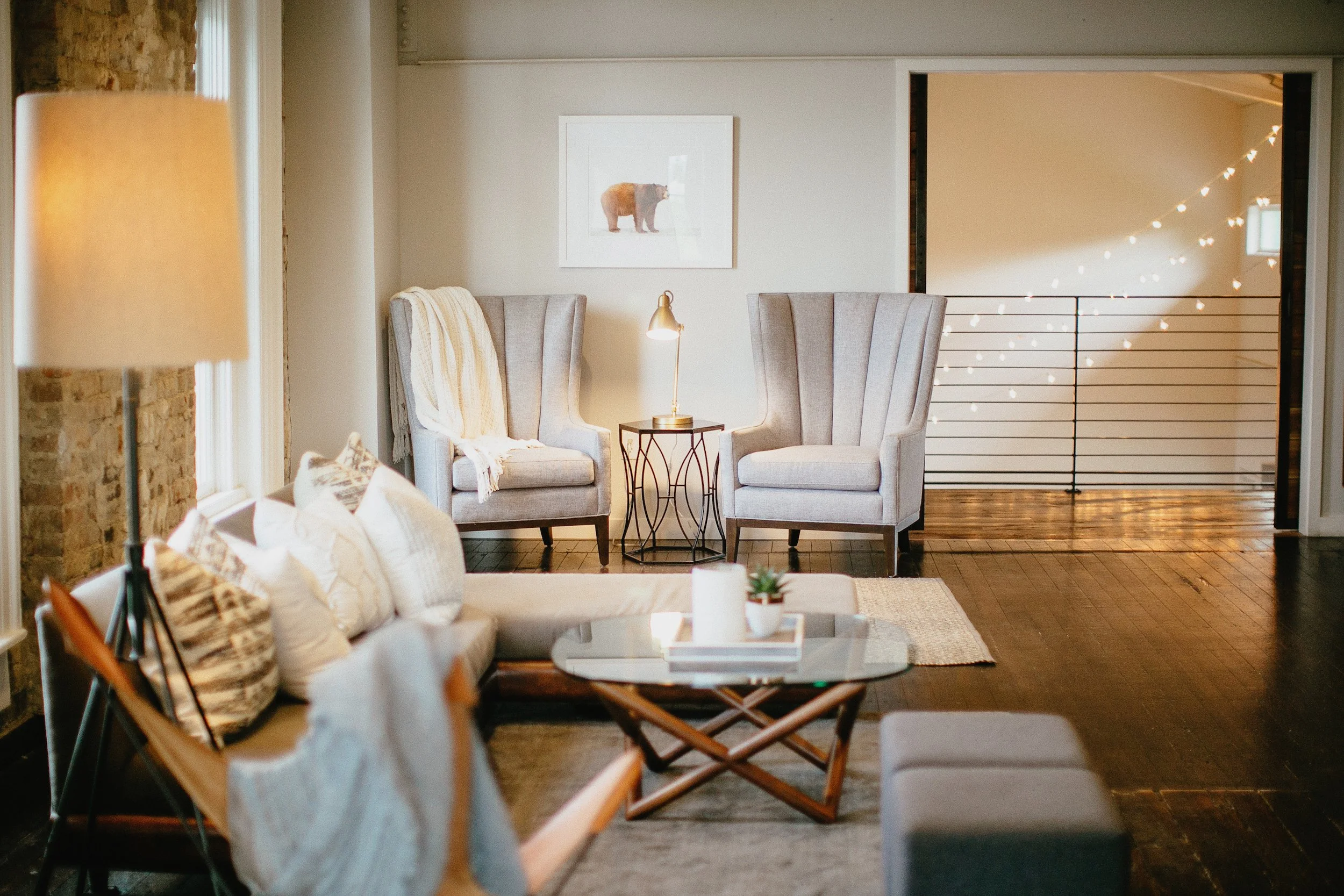 Cordelle Loft Living room with light gray armchairs, a small side table with a lamp, a framed bear picture on the wall, and a window with natural light.