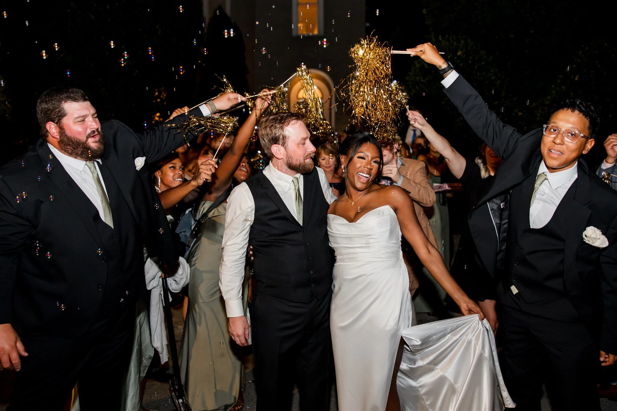 Wedding reception send-off at the Cordelle in Nashville a group of people at a wedding celebration, with some holding gold-colored tinsel decorations, smiling and dressed in formal attire.