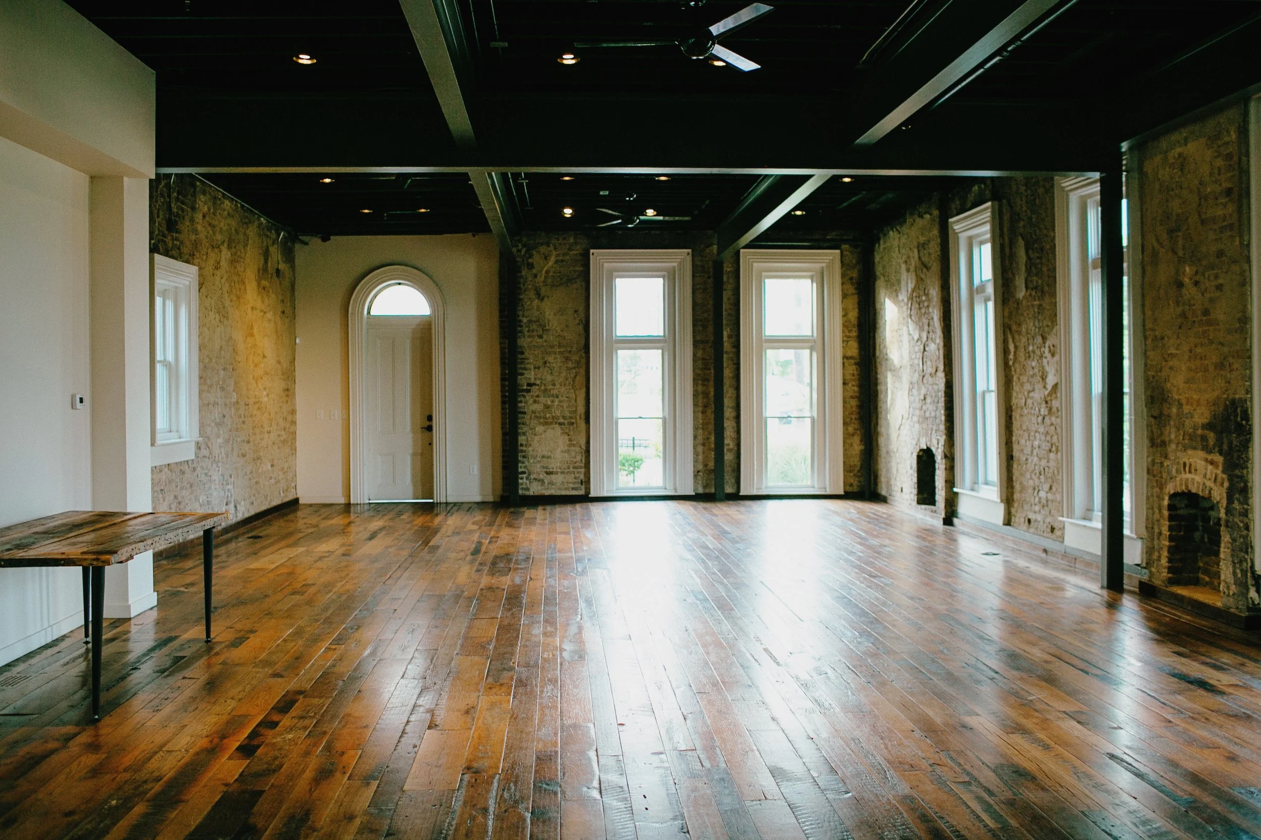 The Victorian at the Cordelle with exposed brick walls, hardwood floors, large windows, and a high ceiling with black beams.