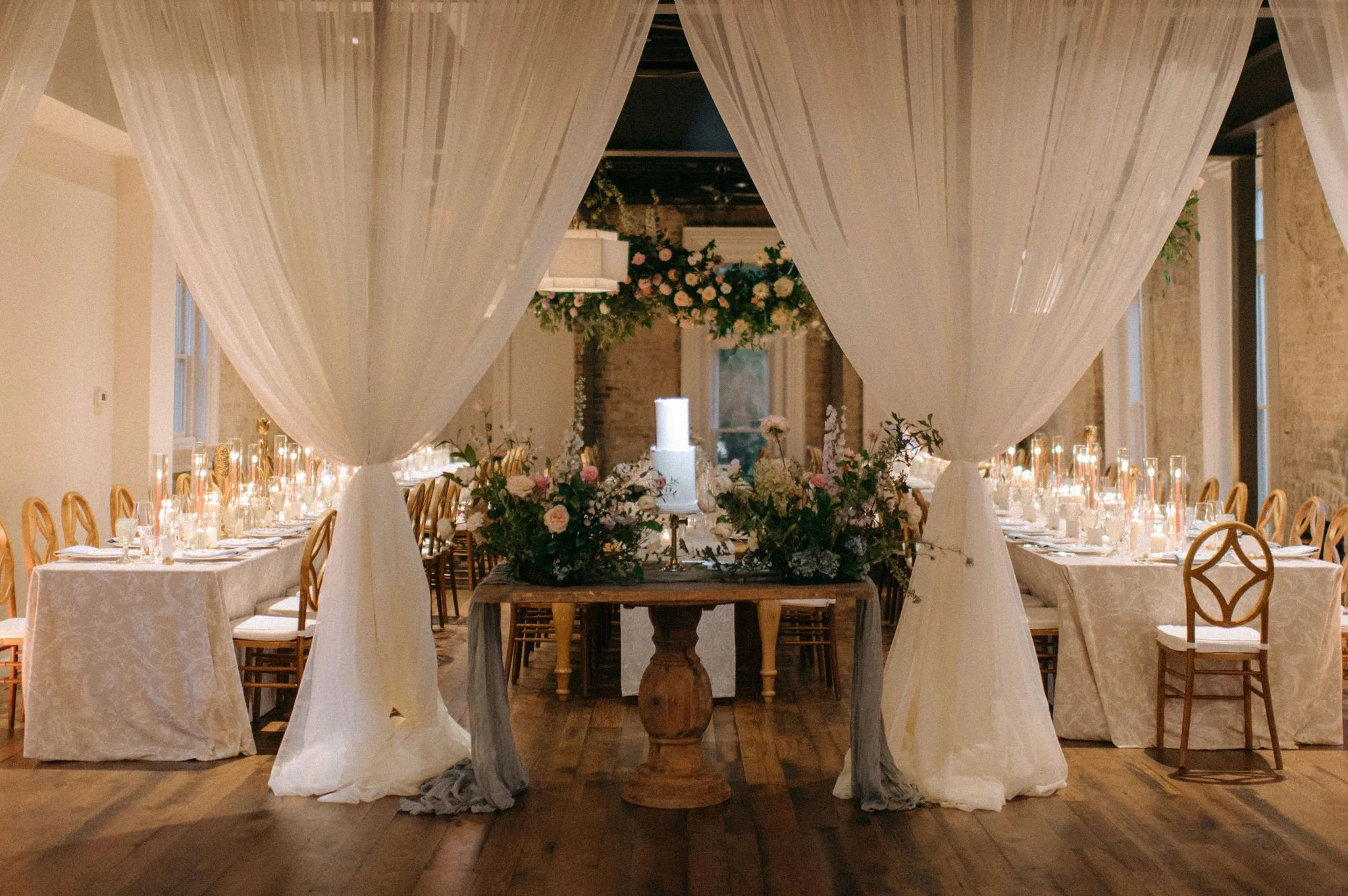 A decorated event space in Downtown Nashville with a long table set with glassware, candles, and floral arrangements. The space features flowing white drapes hanging from above, creating a canopy over the table. 