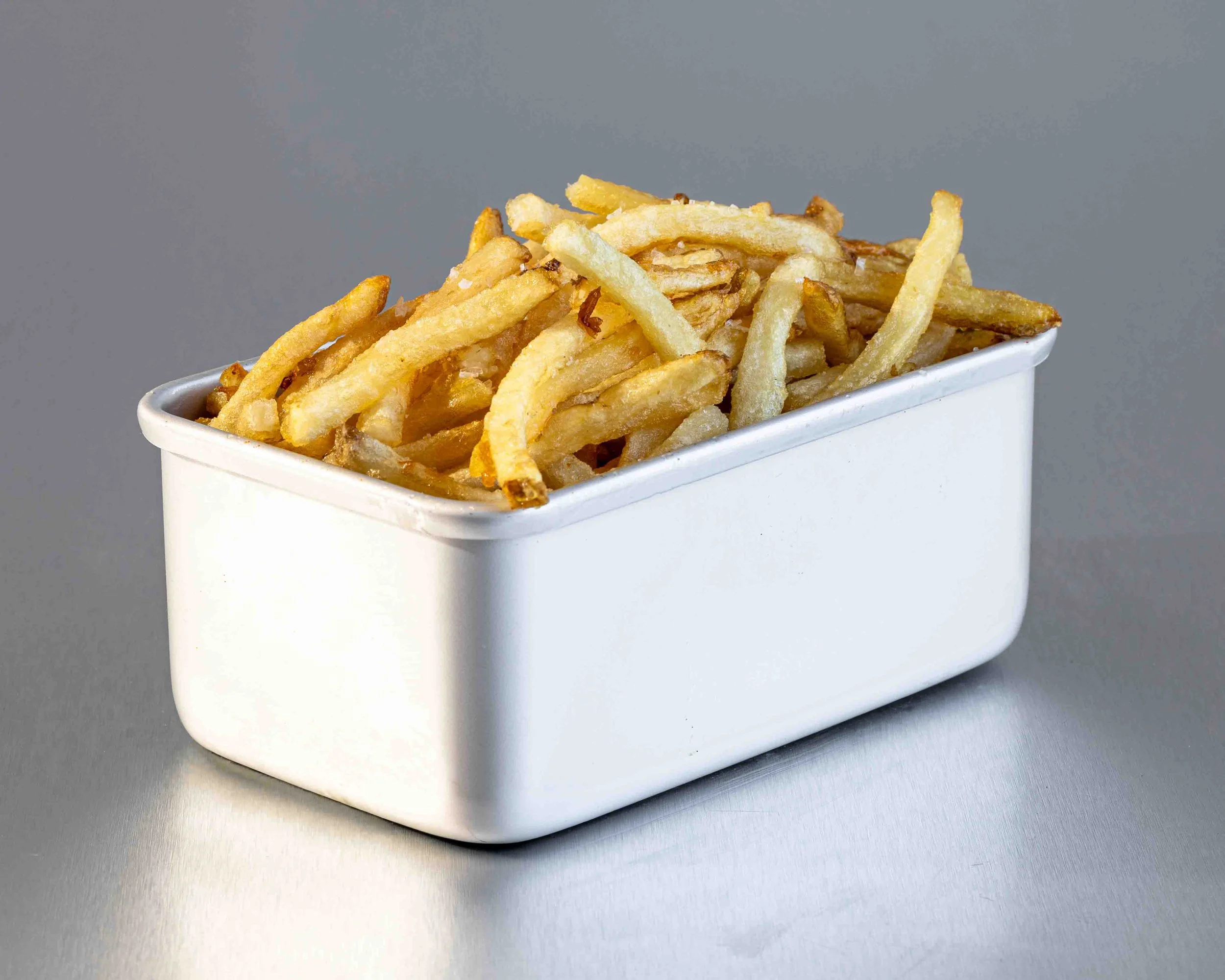 A white container filled with French fries on a metallic surface against a plain gray background.