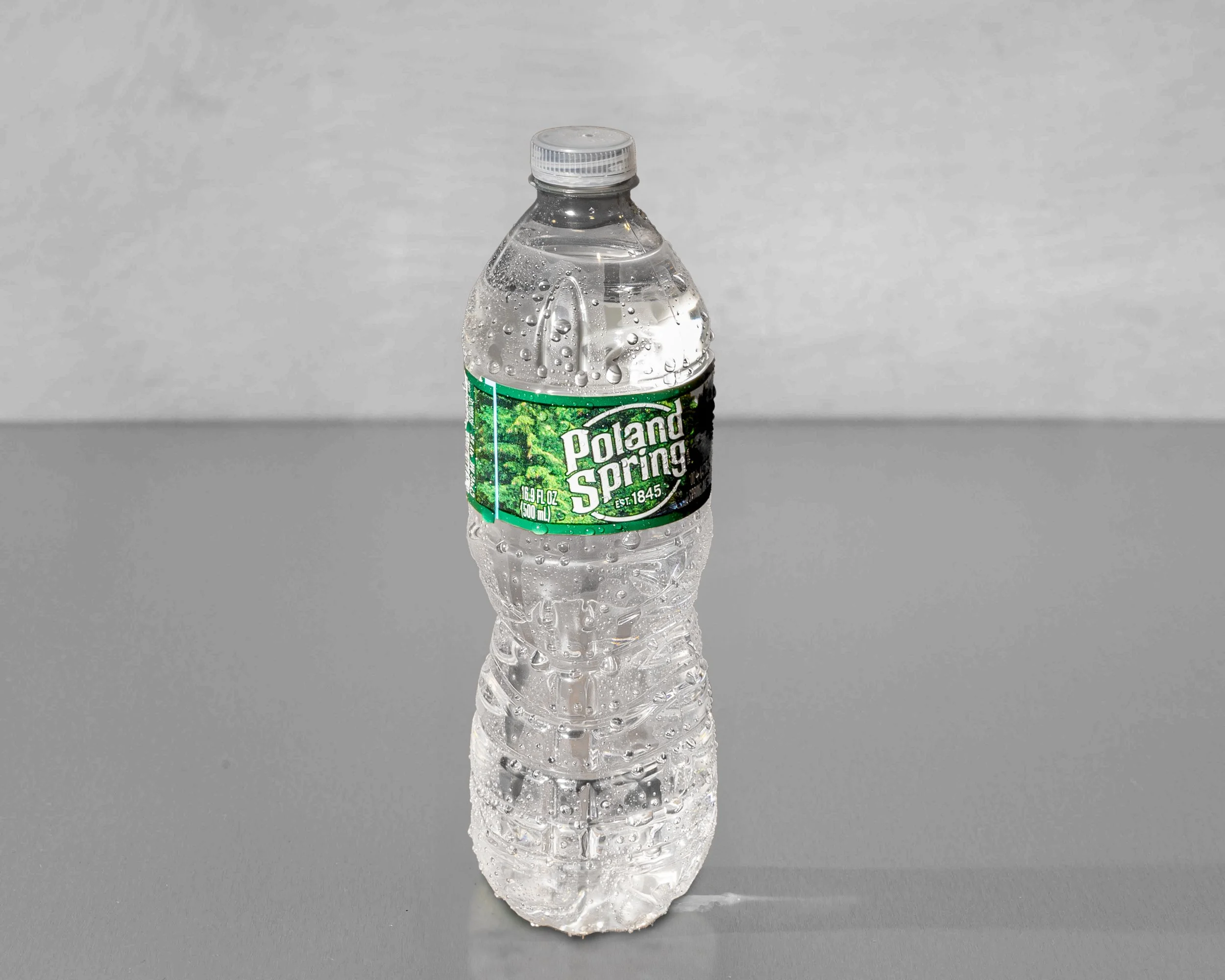 A clear plastic Poland Spring water bottle with condensation drops on it, standing upright on a flat surface against a plain gray background.