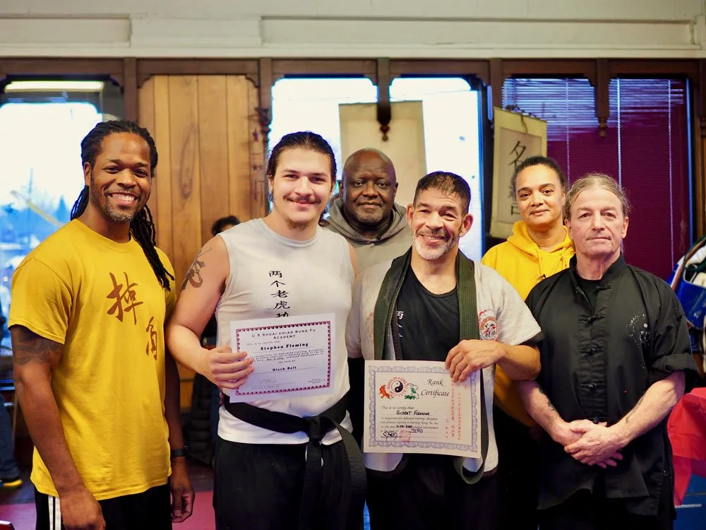 Group of six people, two holding certificates, in a martial arts training area.