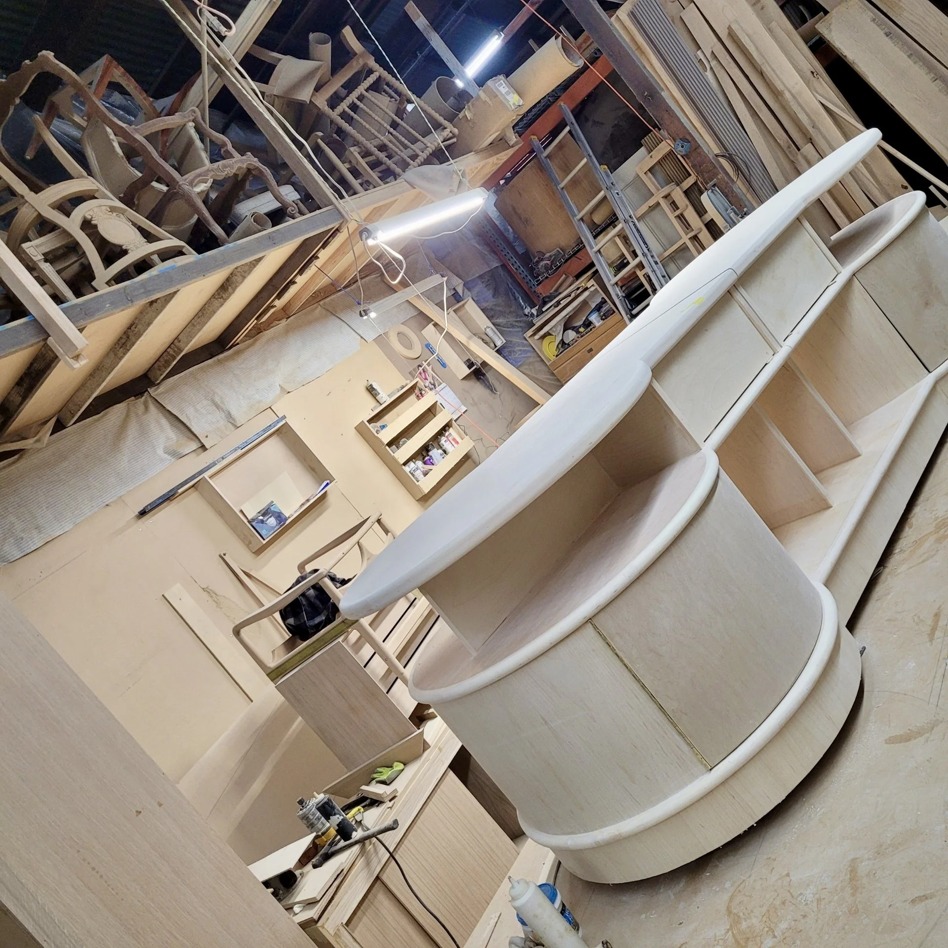 Woodworking shop with various chairs and tools, wooden shelves, and supplies for furniture making.