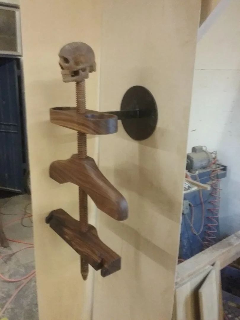 A wooden wall-mounted cat climbing structure with a small skull sculpture on top.