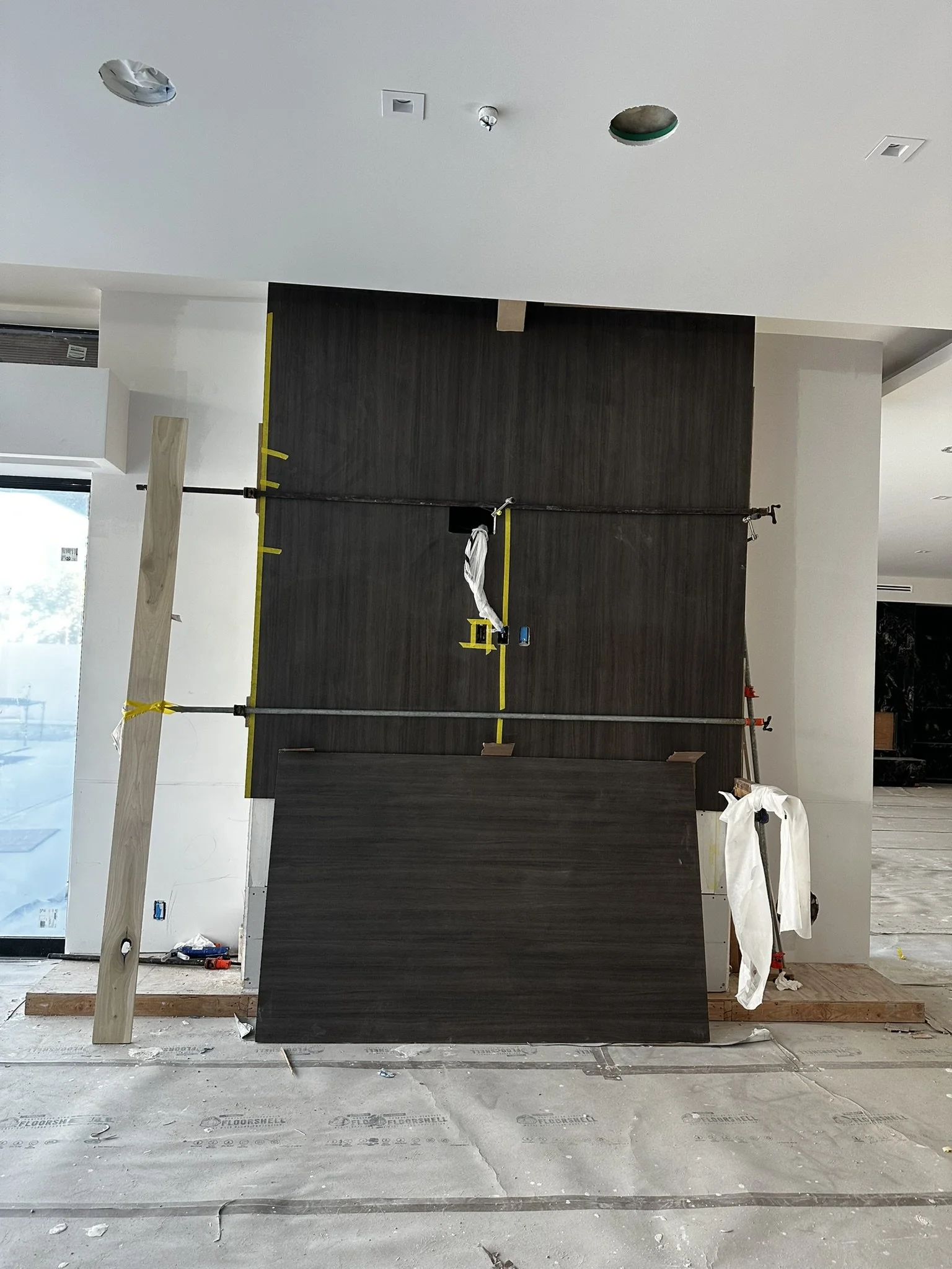 Interior of a building under construction with dark wood panels being installed on a wall, scaffolding, tools, and construction materials scattered on the floor.