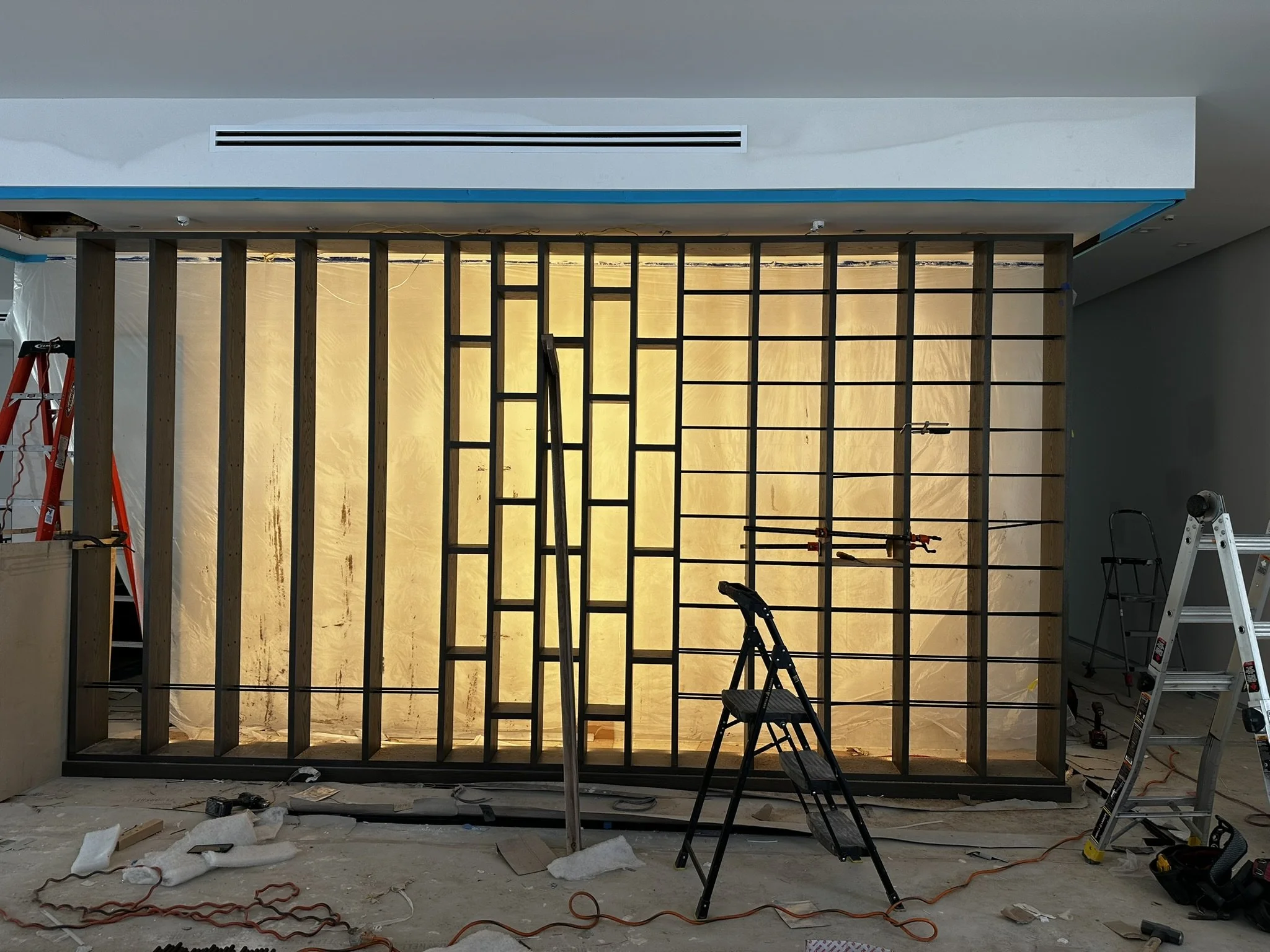 Construction site with a partially built wall, ladders, tools, and wiring, and a yellow backdrop behind the wall.