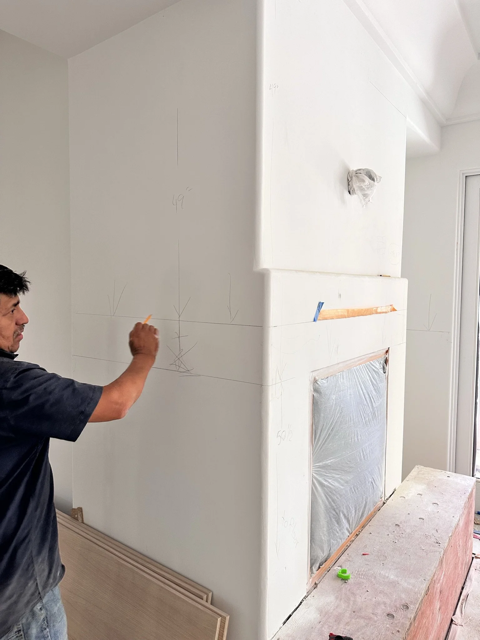 Person working on drywall in a room under construction, with drywall markings and taped corners.